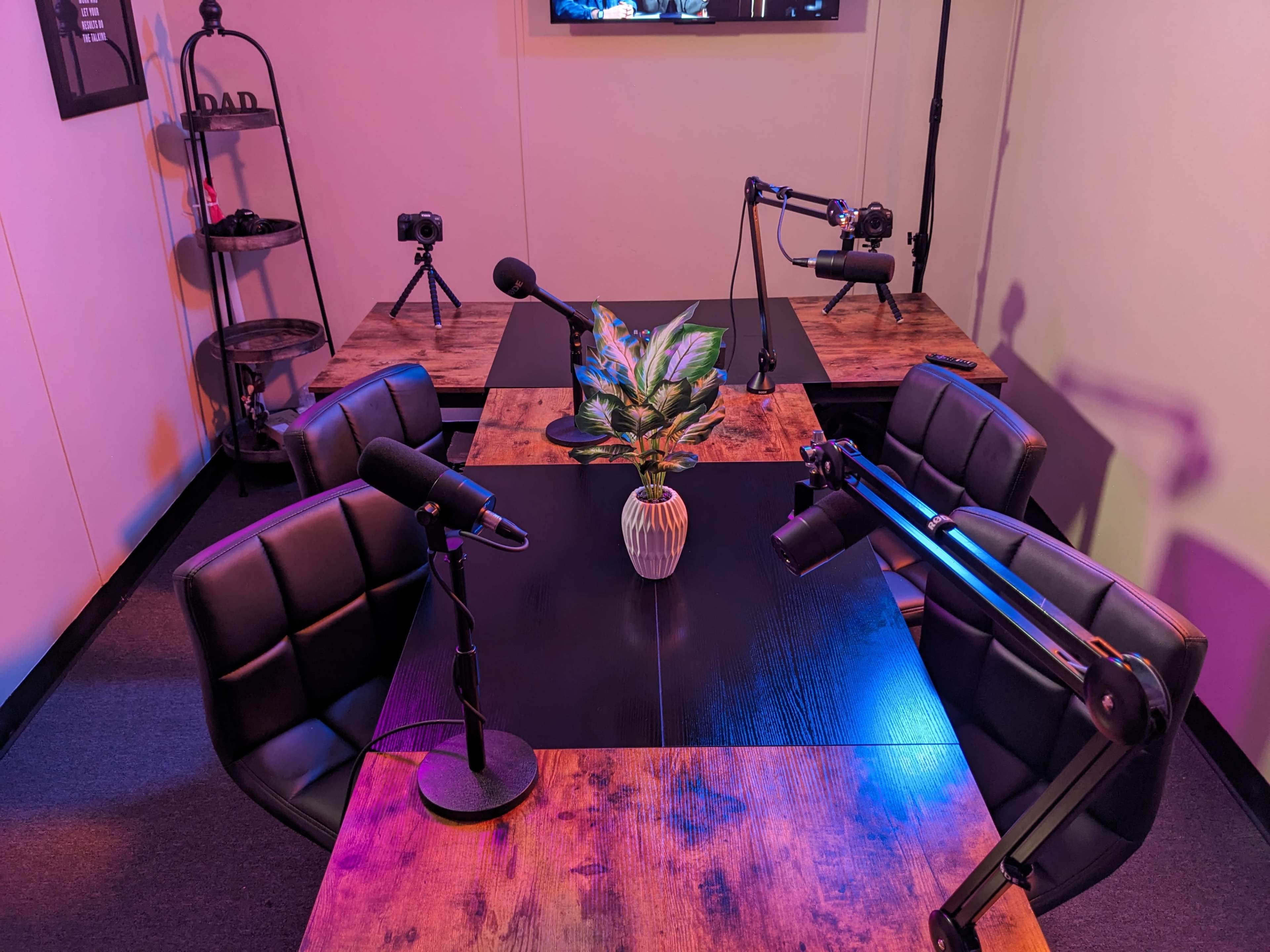 A podcast recording setup features four chairs around a table, with microphones and cameras positioned for recording.