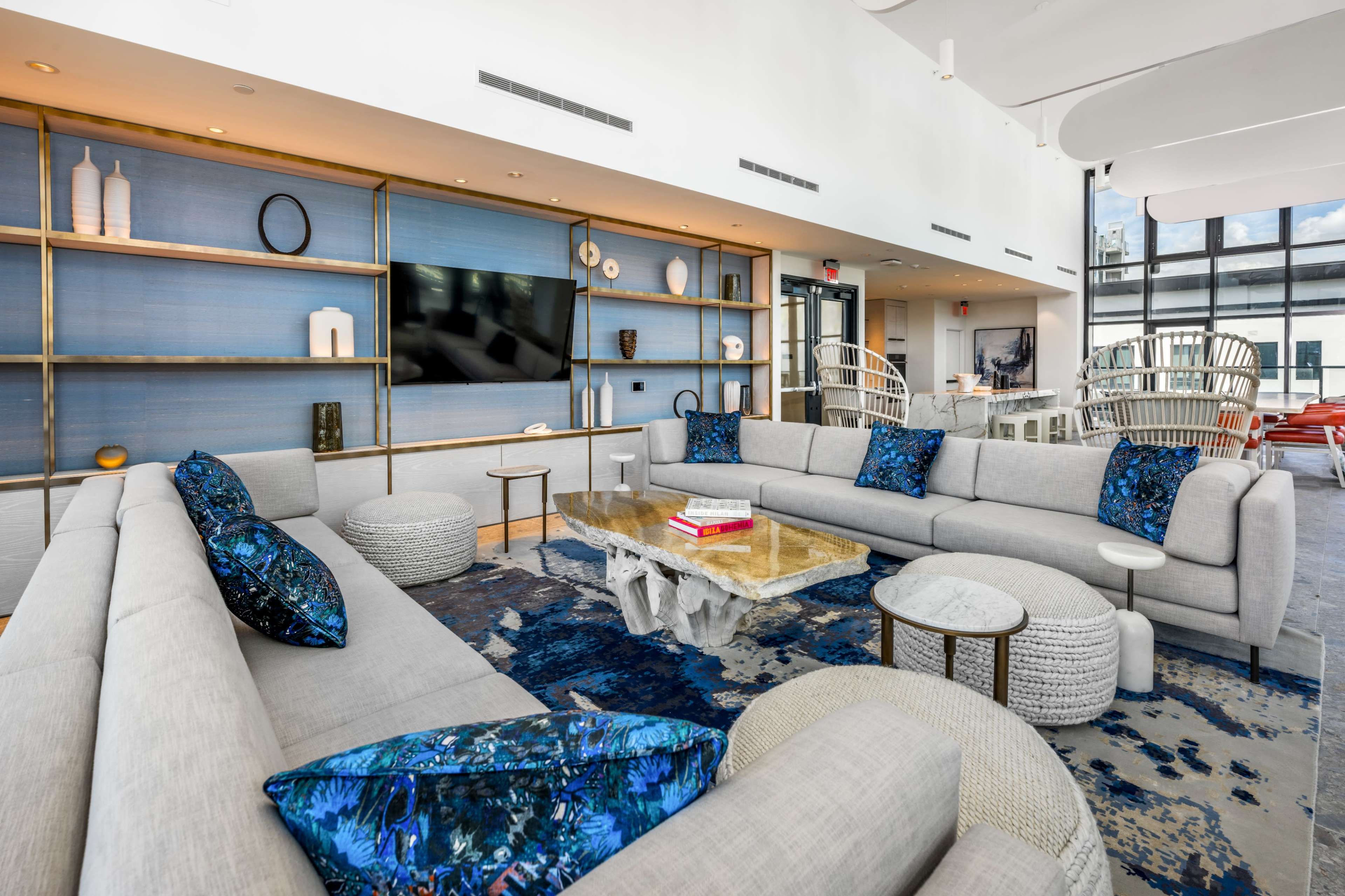 A modern living space features a curved sectional sofa, a coffee table made of stone, and decorative accents on shelves, with large windows allowing natural light to enter.