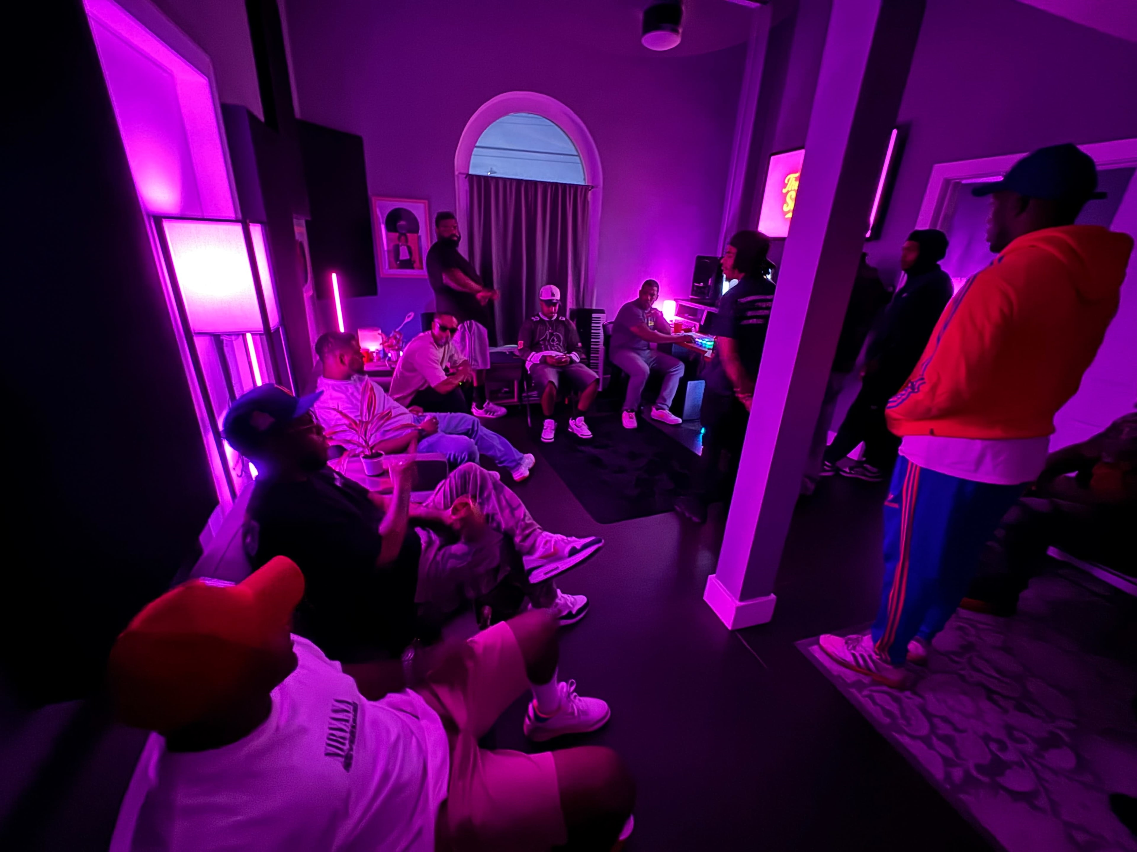 A group of individuals is gathered in a dimly lit room with purple lighting, engaged in conversation and socializing.