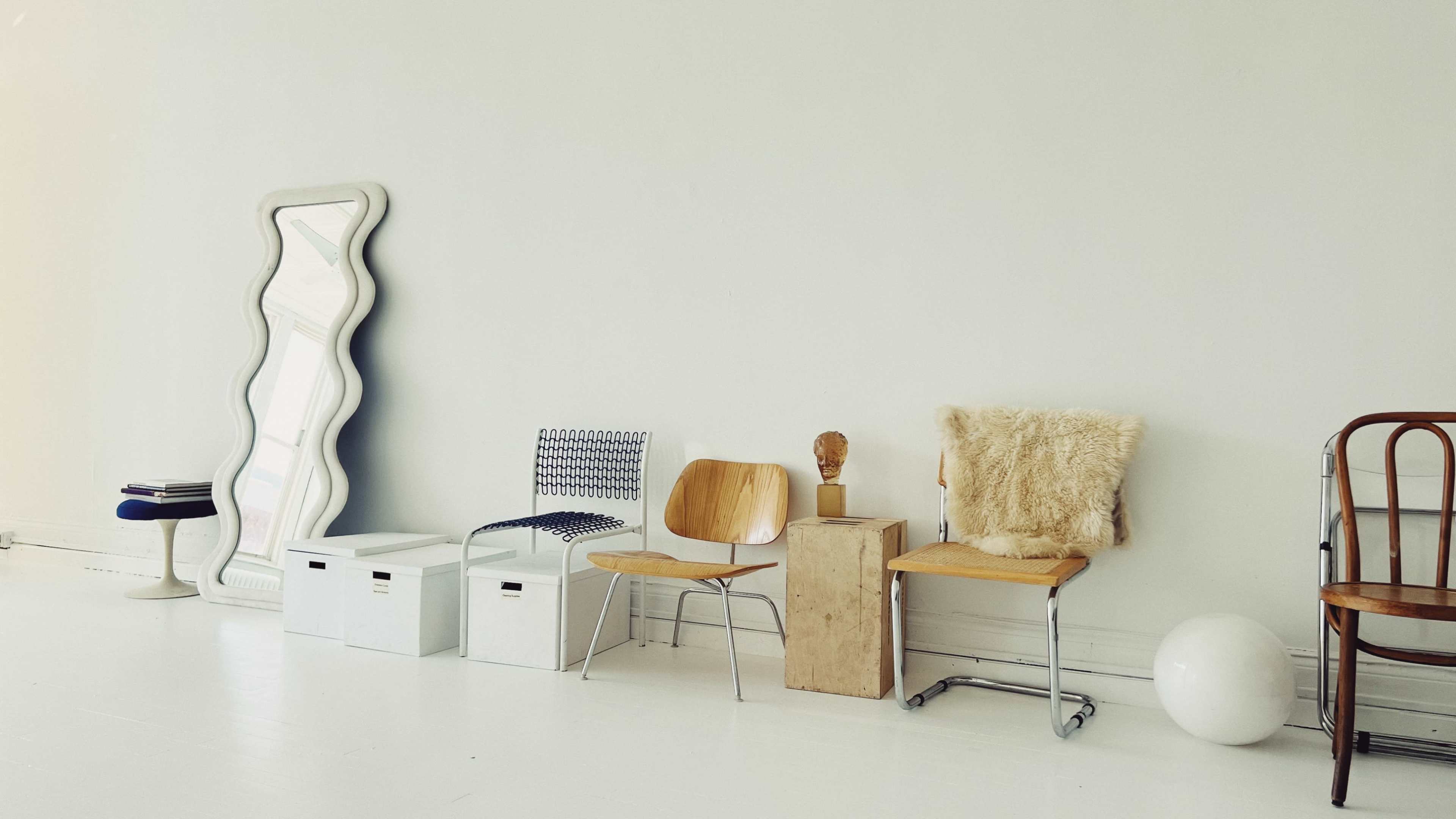 A row of various chairs and decorative items is positioned against a plain white wall in a minimalist space.