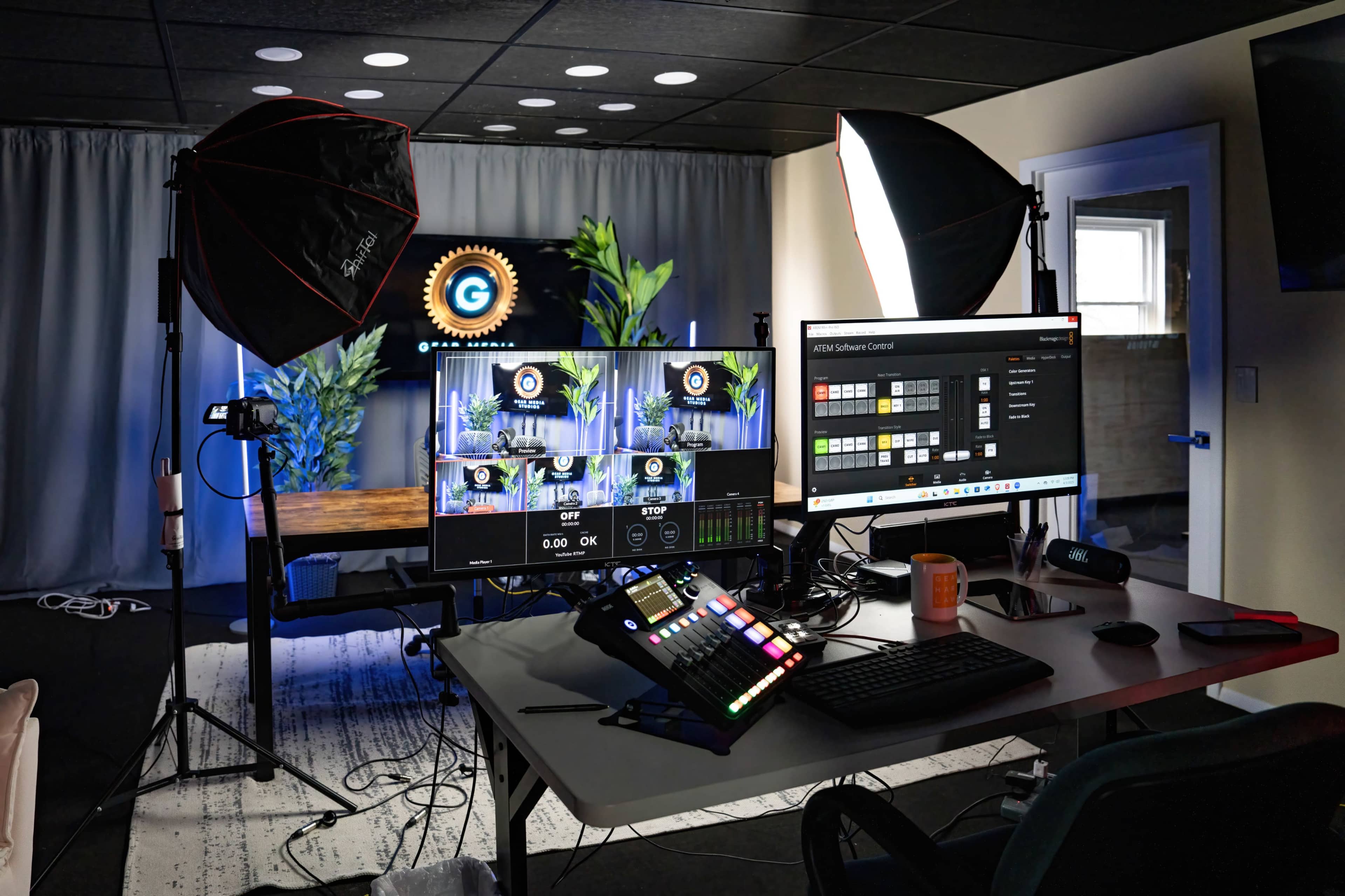 The image shows a modern video production setup with multiple monitors, a control panel, and lighting equipment in an office-like space.