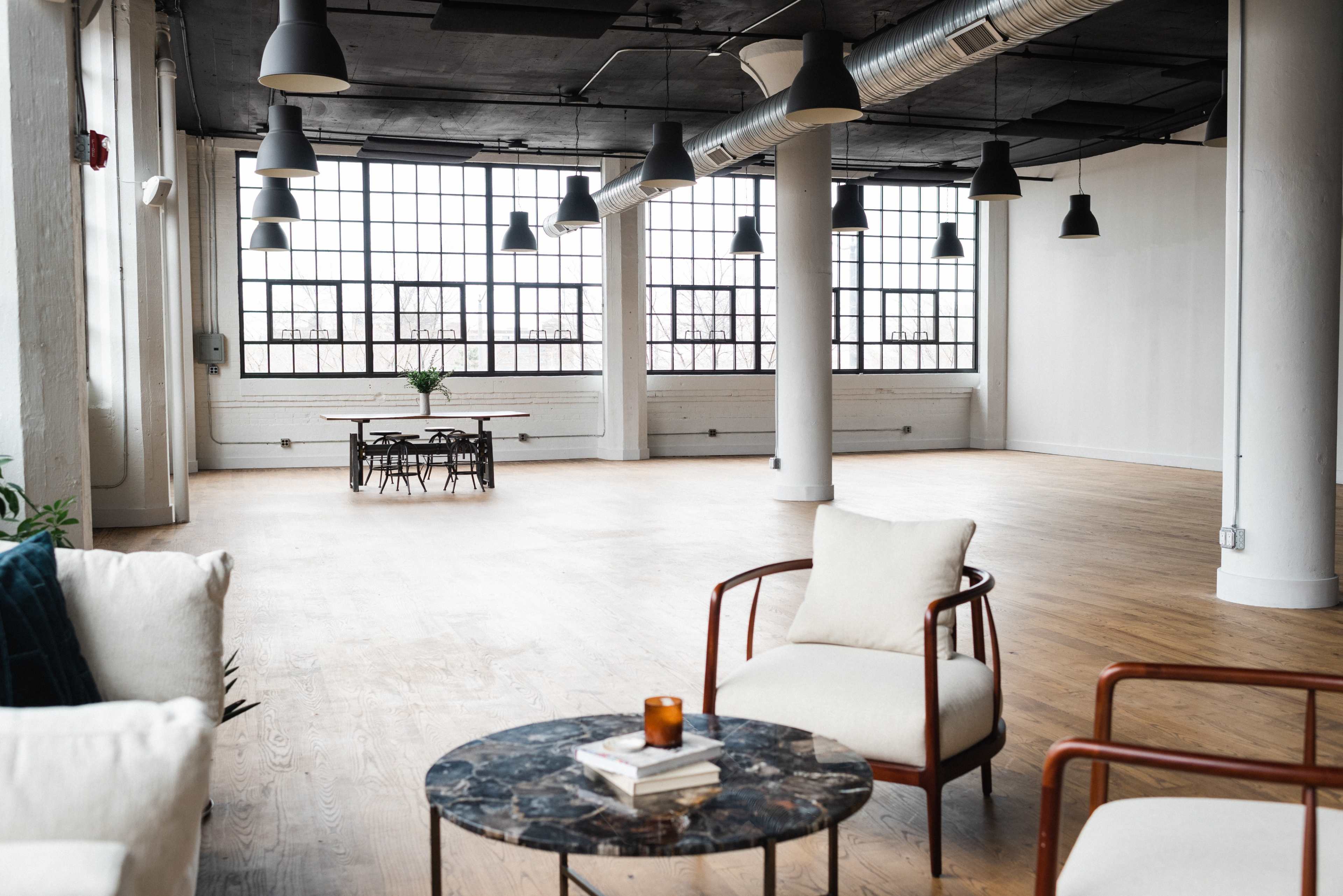 A spacious, modern interior with large windows, minimal furniture, and wooden flooring.