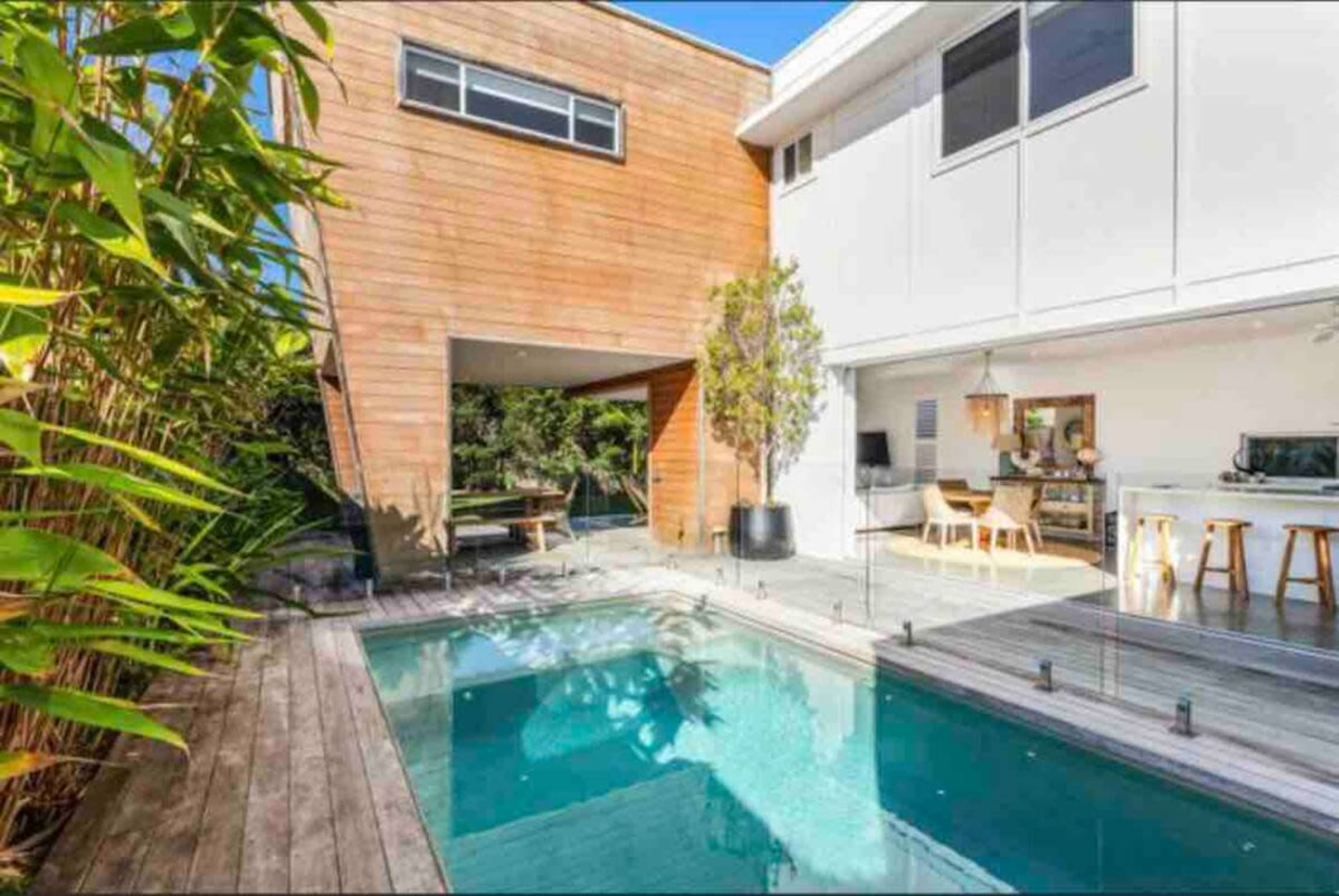 A modern home with a wooden exterior, a swimming pool, and a patio area surrounded by greenery.