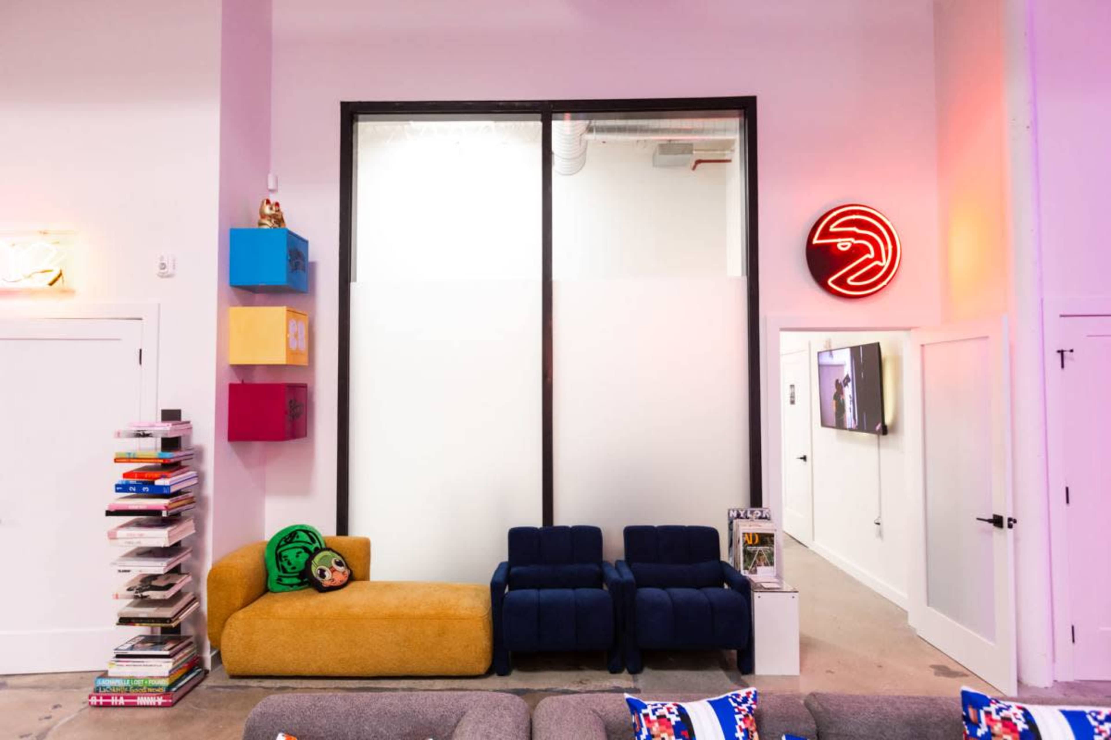 A modern room features a blue couch set, colorful wall-mounted storage boxes, a stack of books, and a neon sign.
