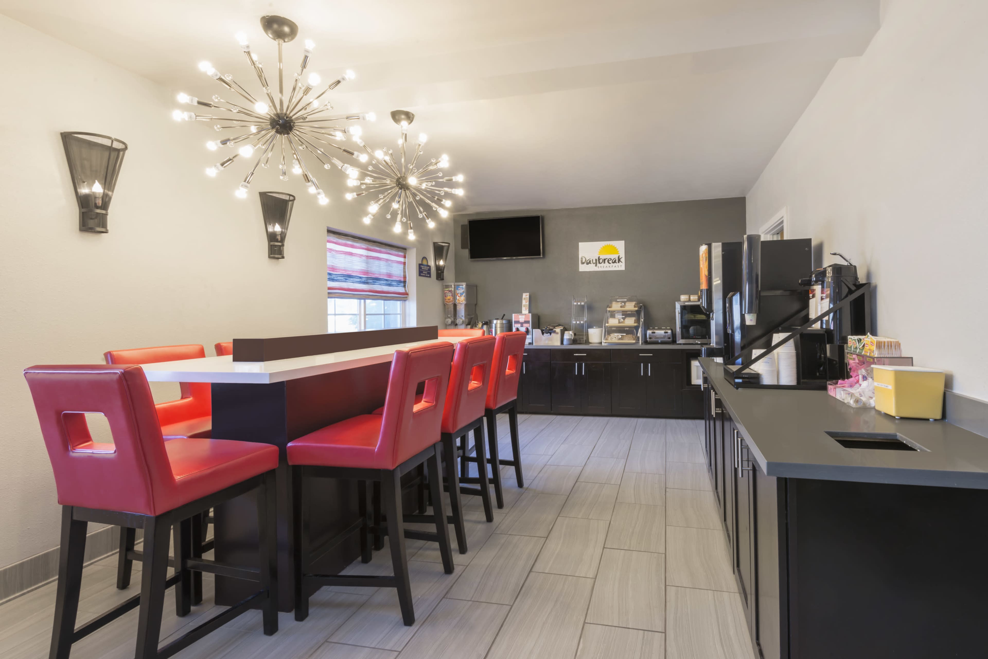 A modern dining area with high tables and red chairs, a dark cabinetry counter, and decorative light fixtures.
