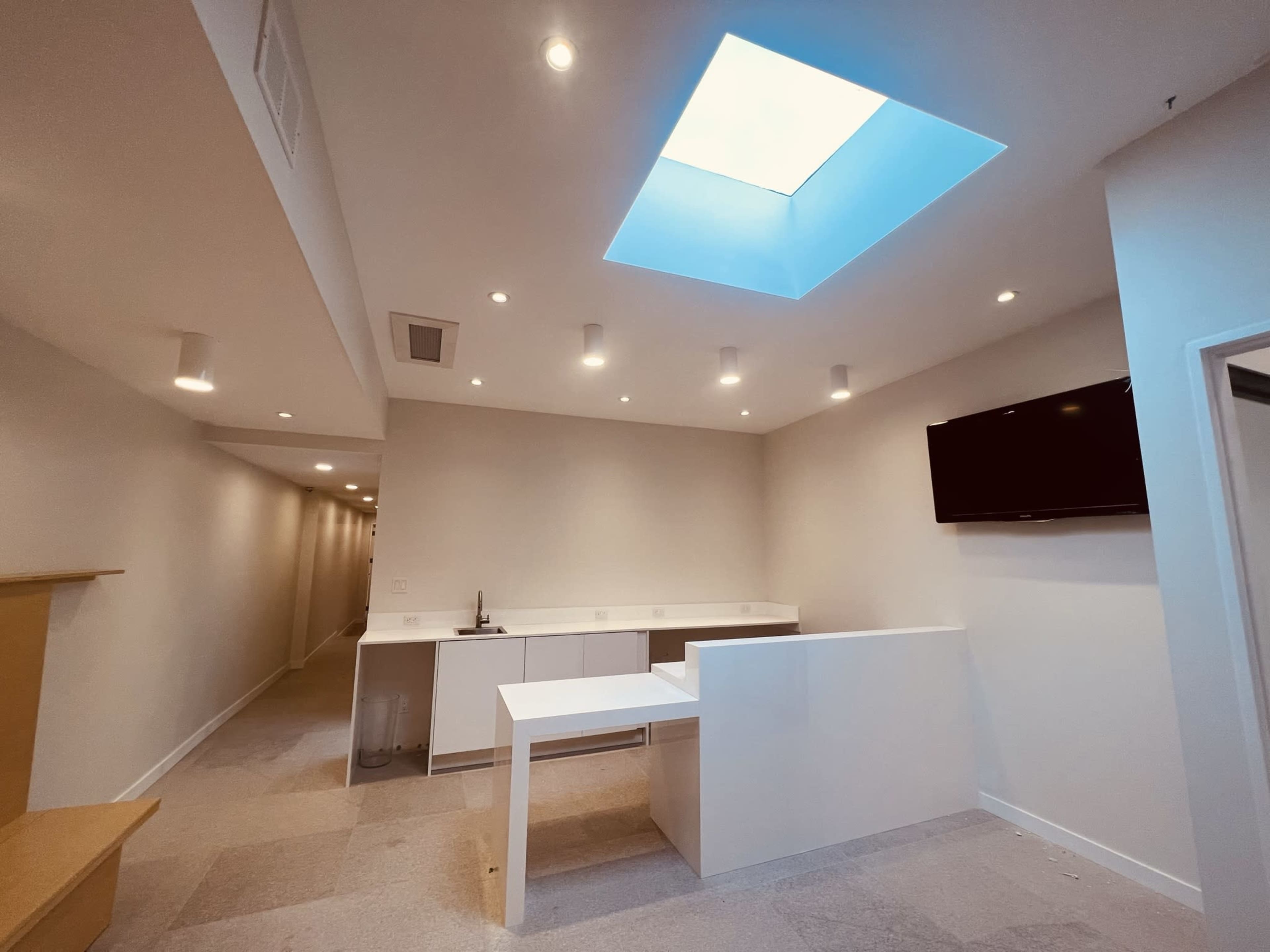 A modern, minimalist room featuring a skylight, a white counter, and a television mounted on the wall.