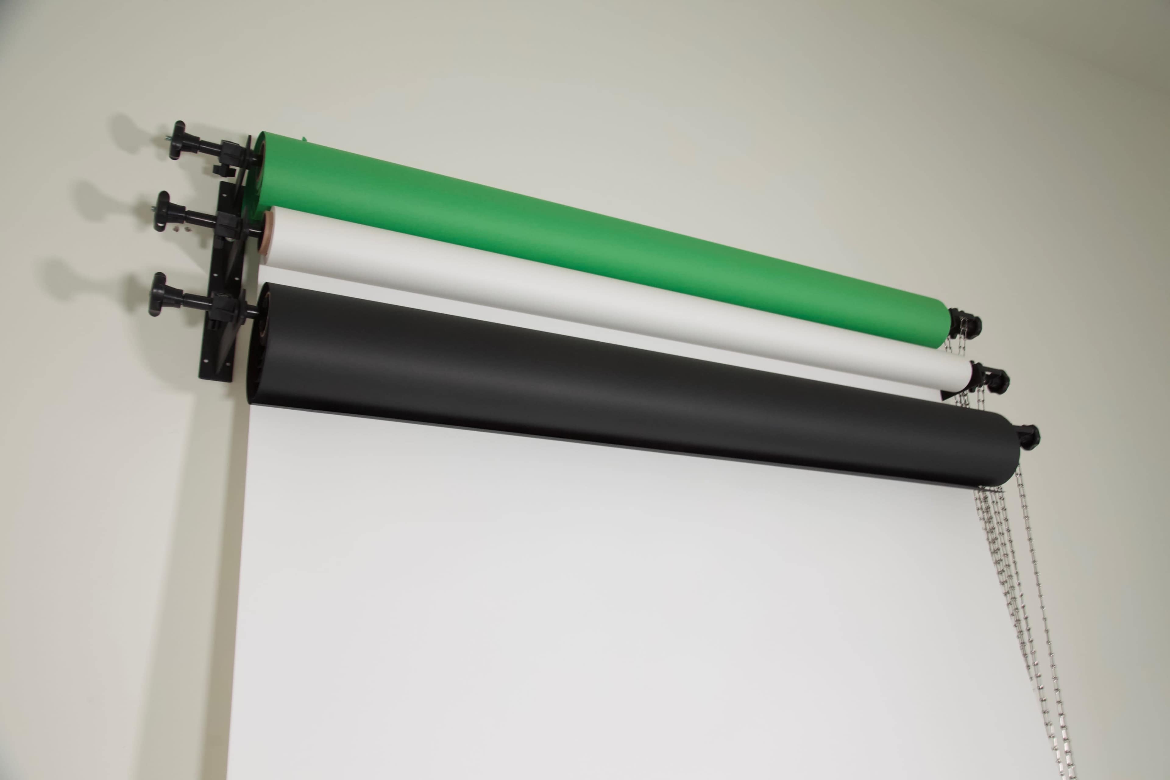 Three rolls of backdrop paper in green, white, and black mounted on a wall.