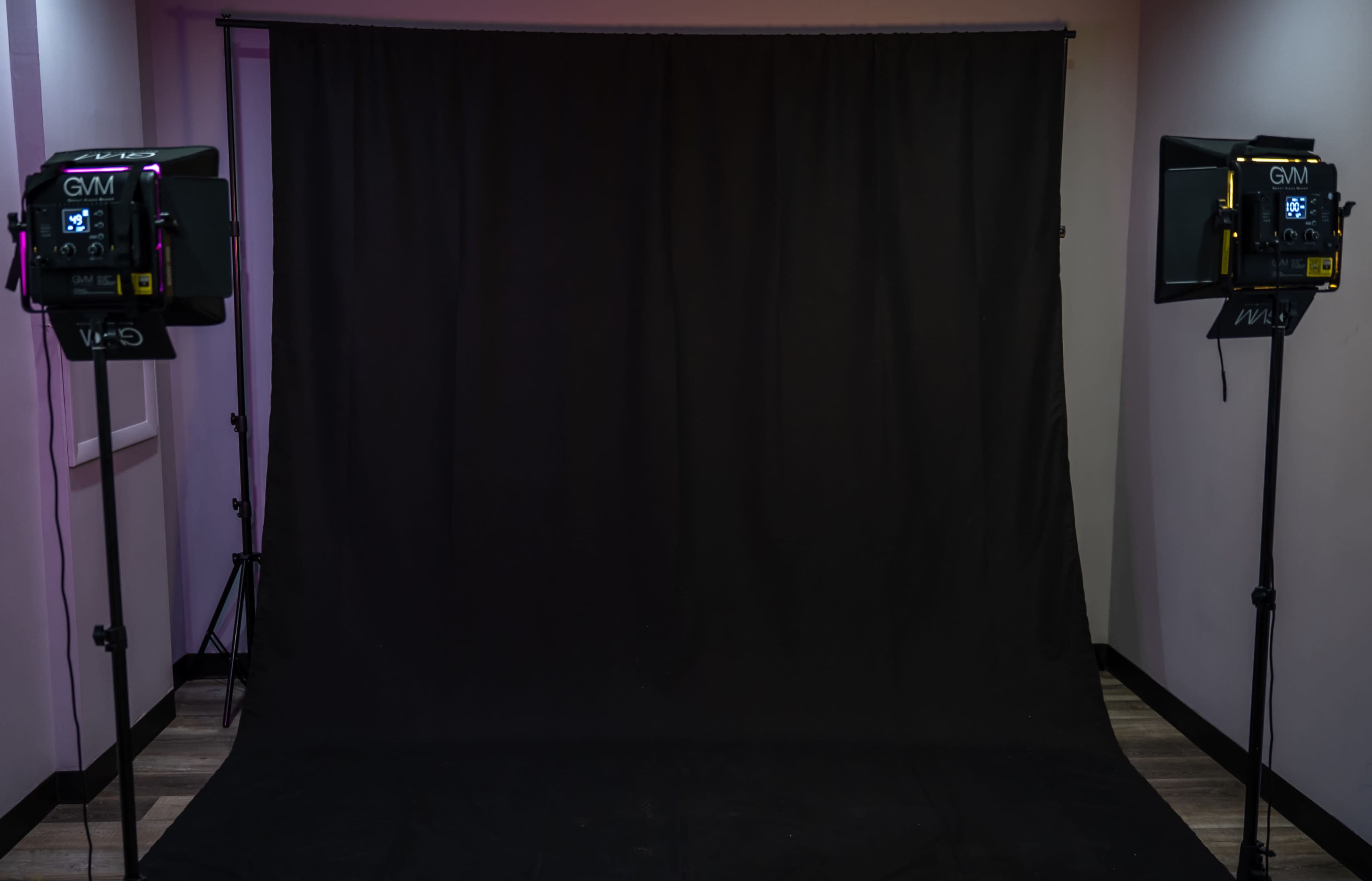 A photography studio with a black backdrop and two lighting fixtures positioned on either side.