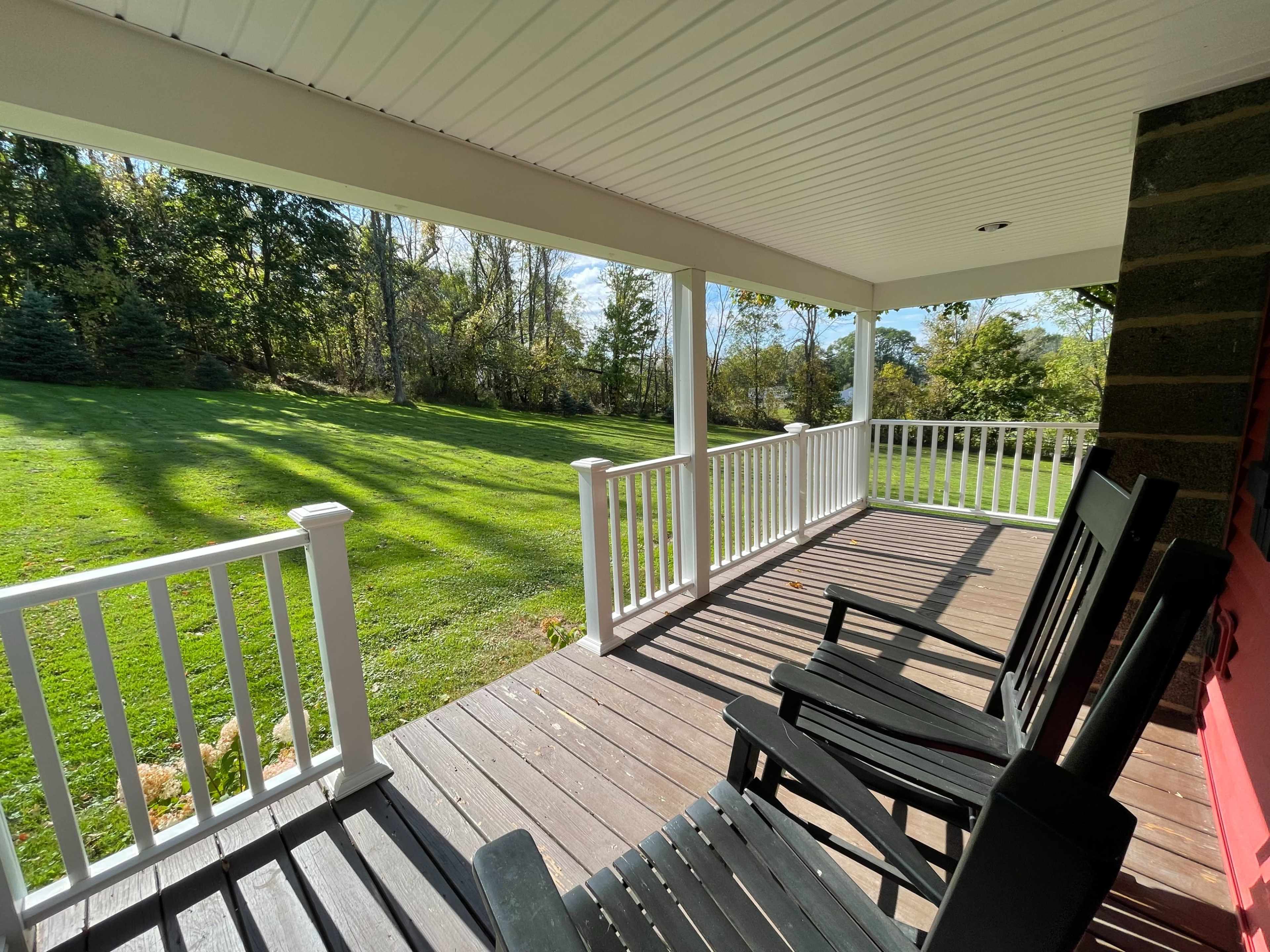 A porch with two rocking chairs overlooks a green lawn surrounded by trees.