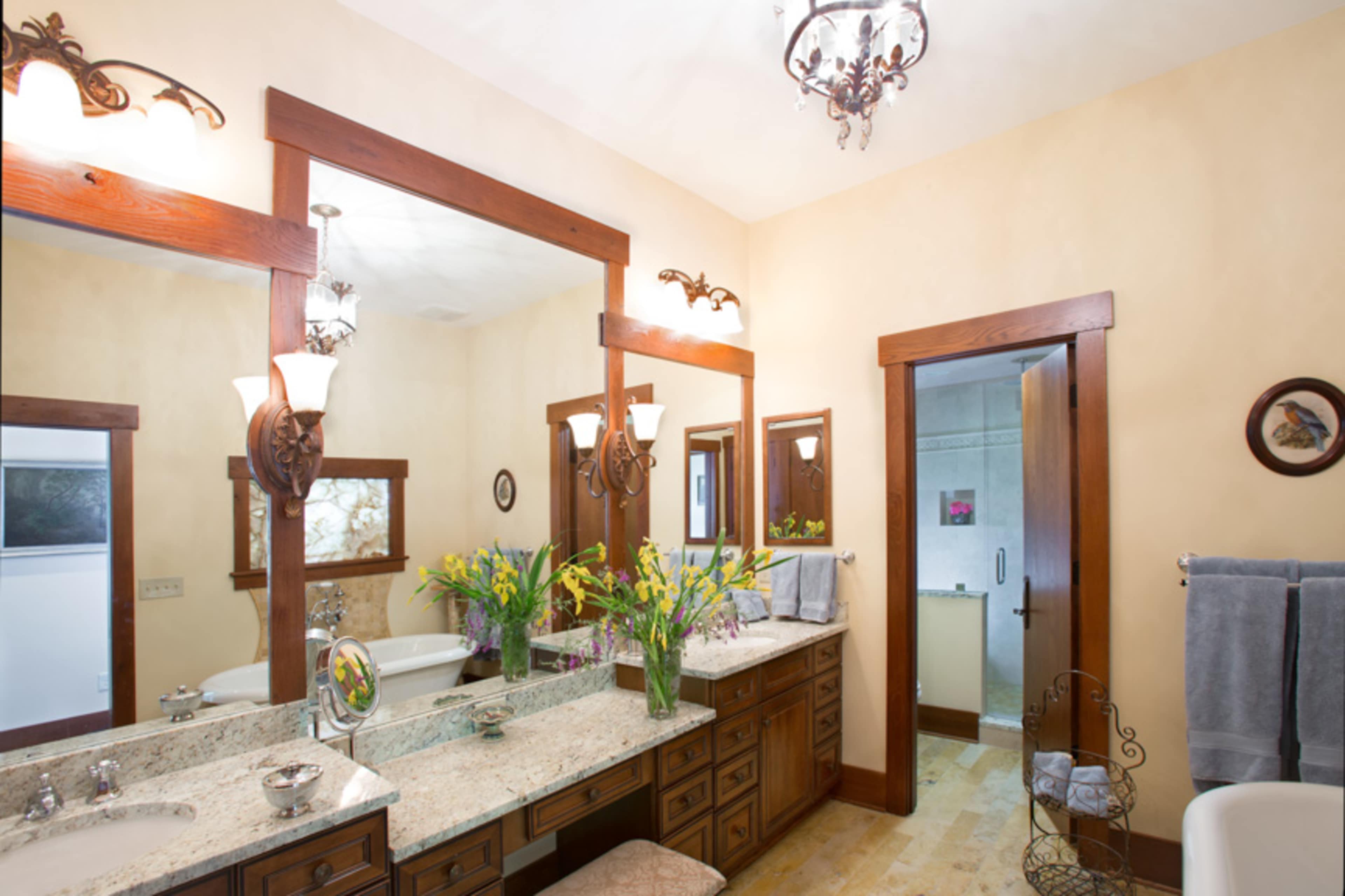 A spacious bathroom featuring dual sinks with a granite countertop, three mirrors, and decorative lighting fixtures.