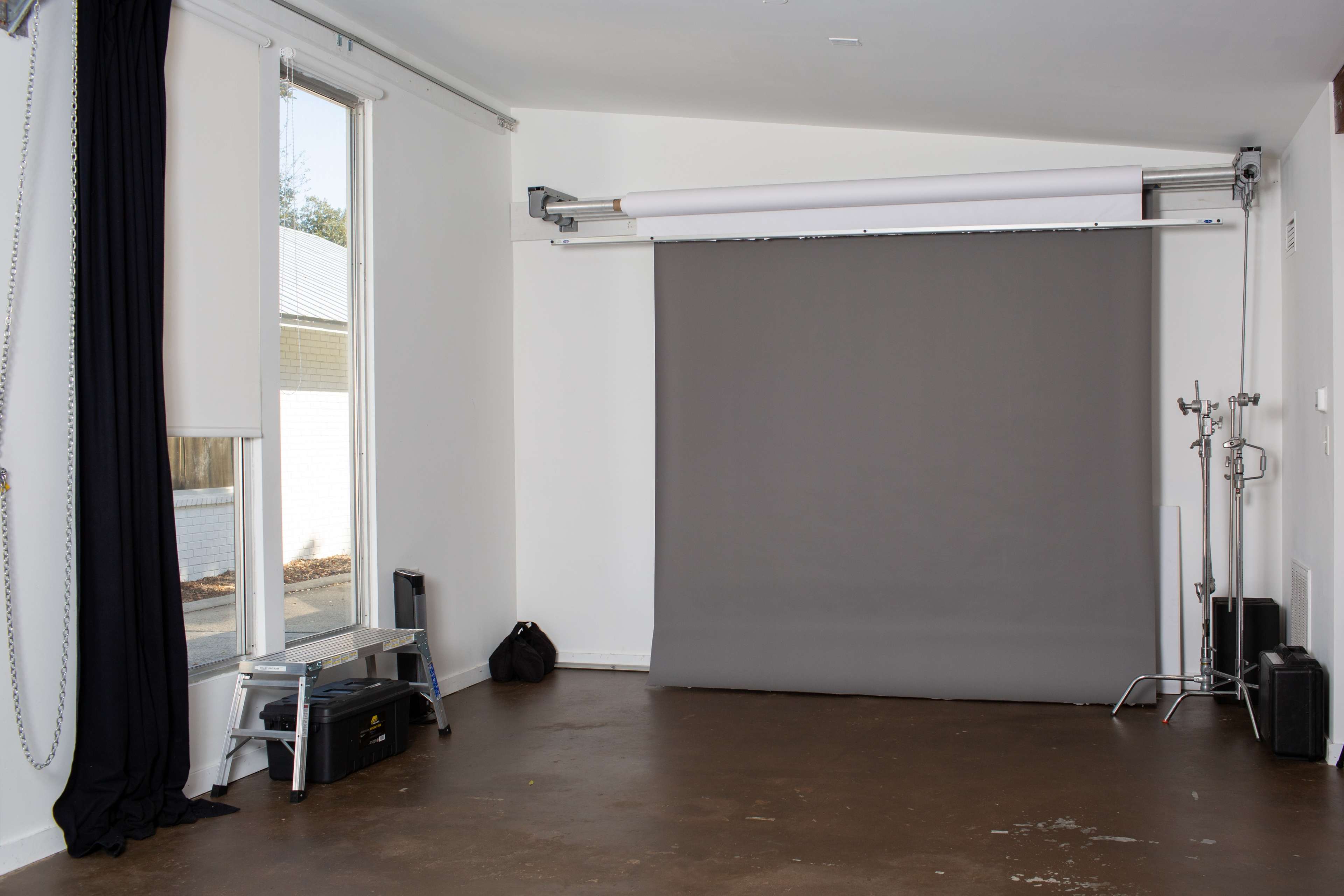 A photography studio with a gray backdrop, large windows, and minimal furnishings.