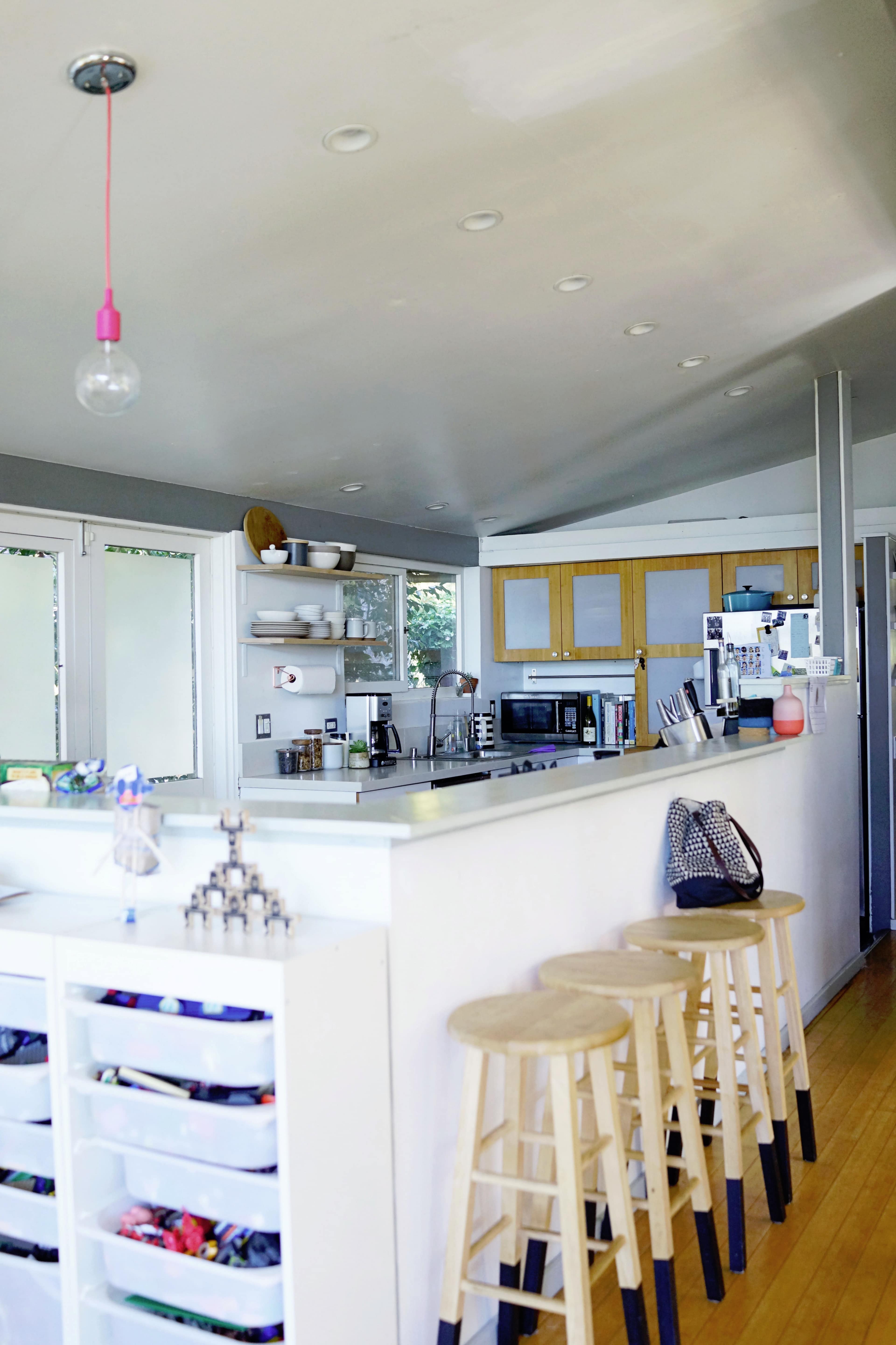 A modern kitchen features a clean design with a central island, bar stools, and shelves displaying dishware and utensils.