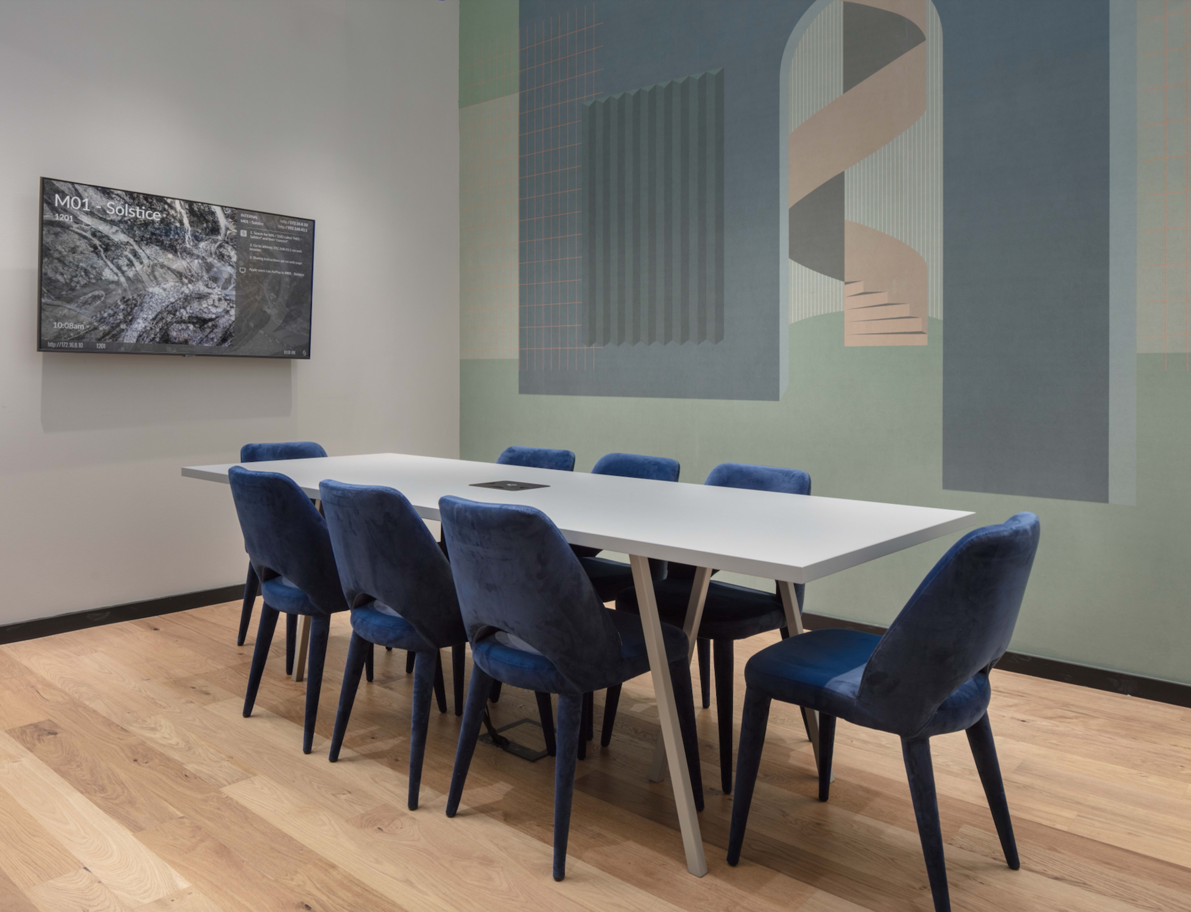 A modern conference room features a long white table with eight blue chairs and a large wall mural with geometric patterns.