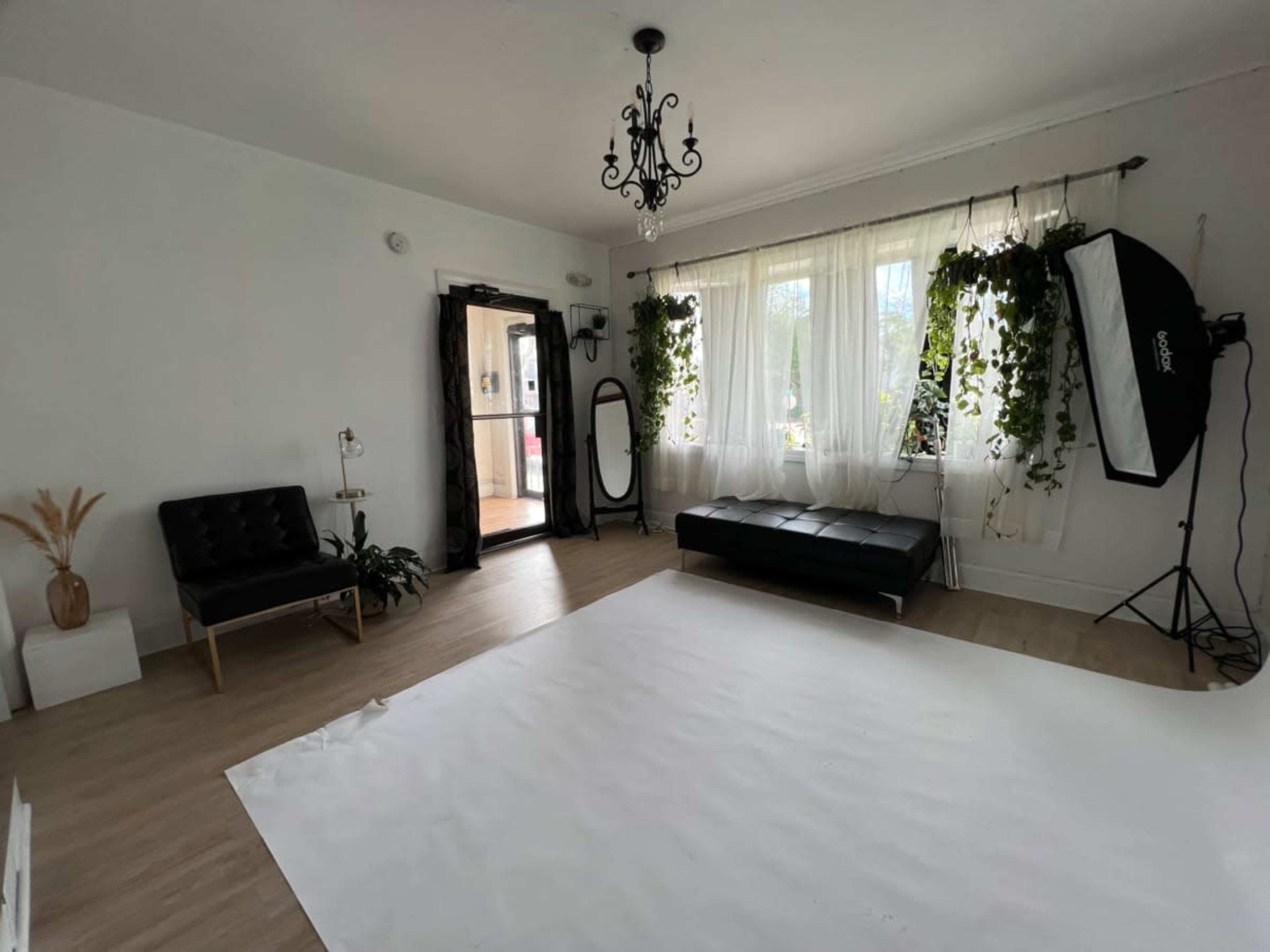 A minimalist studio space featuring a black couch, a large mirror, and soft natural light filtering through sheer curtains.