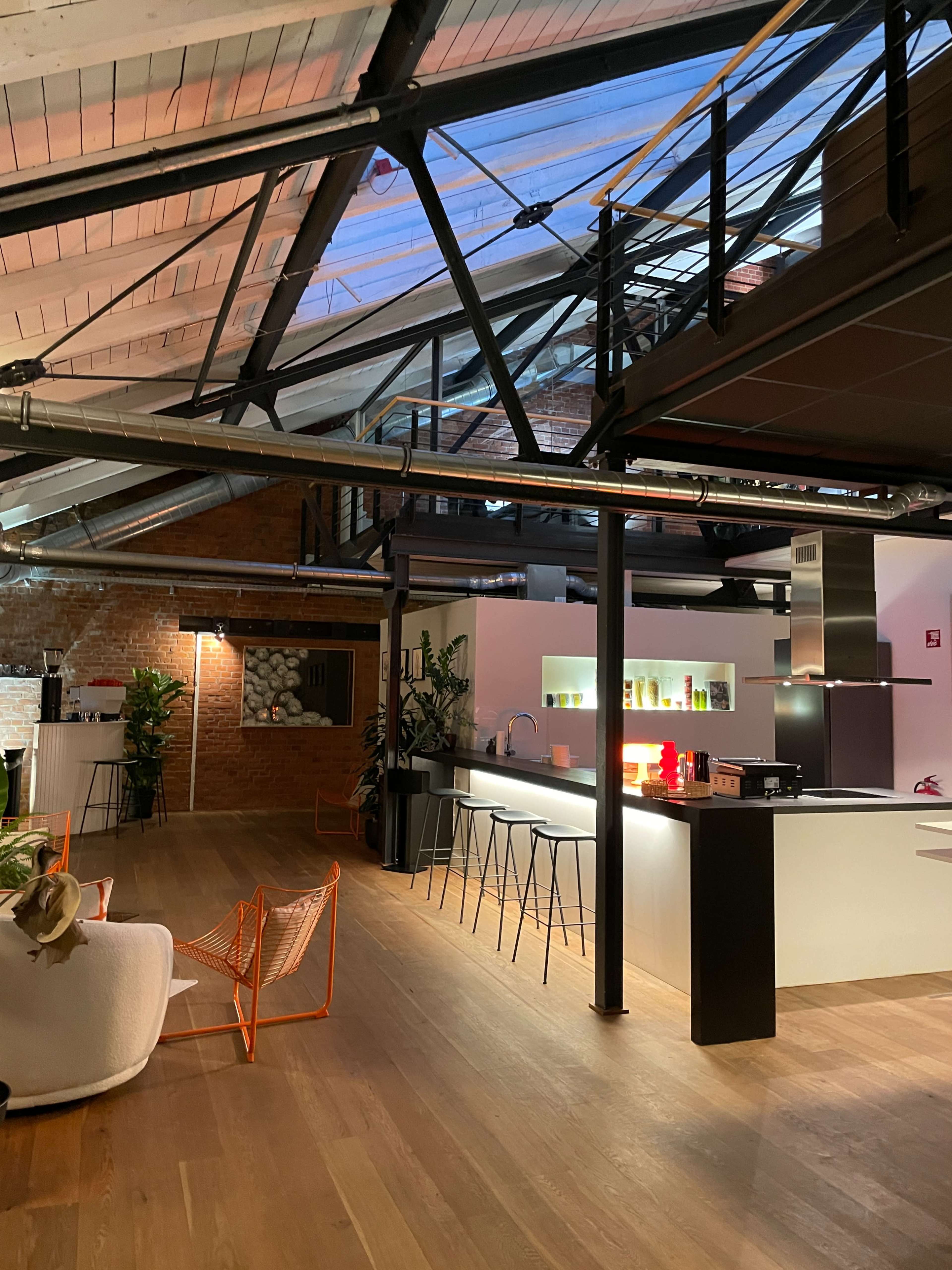 The image shows a modern open-plan interior with a kitchen, seating area, and exposed beams in a loft space.