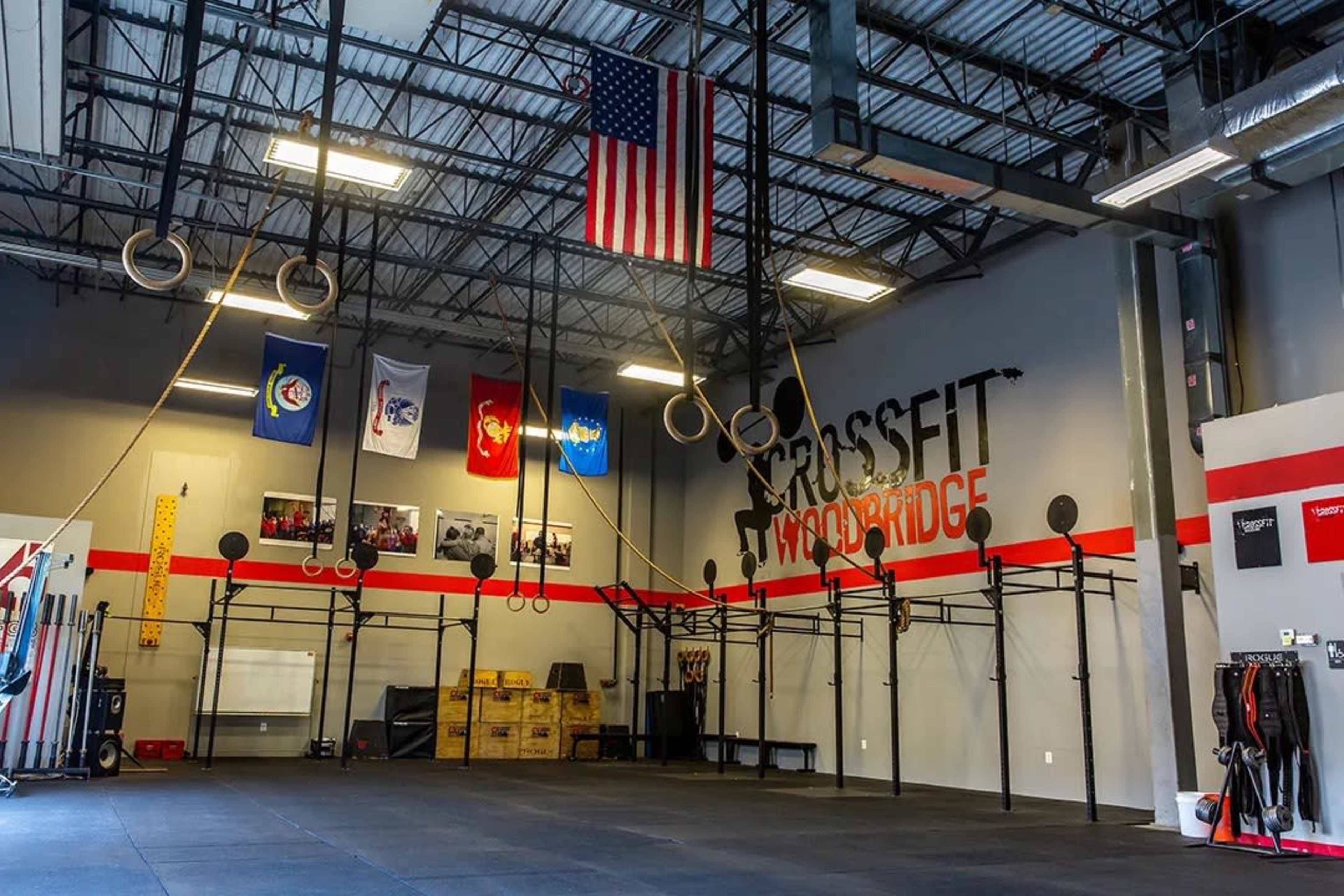 The interior of a CrossFit gym with gymnastic rings hanging from the ceiling and various flags displayed on the walls.