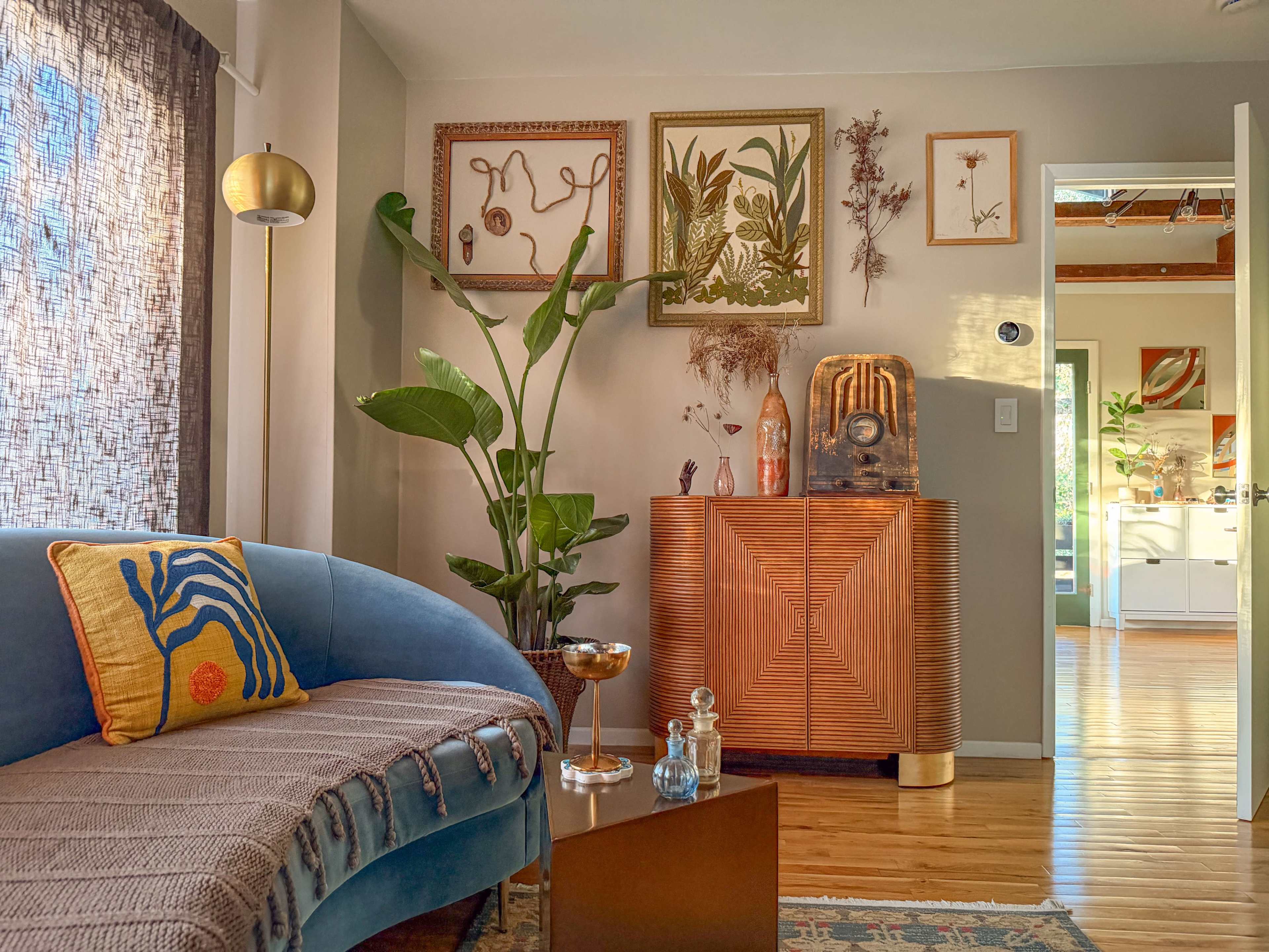A cozy living room features a blue curved sofa adorned with a decorative pillow, a potted plant, and a cabinet displaying framed artwork and decorative items.