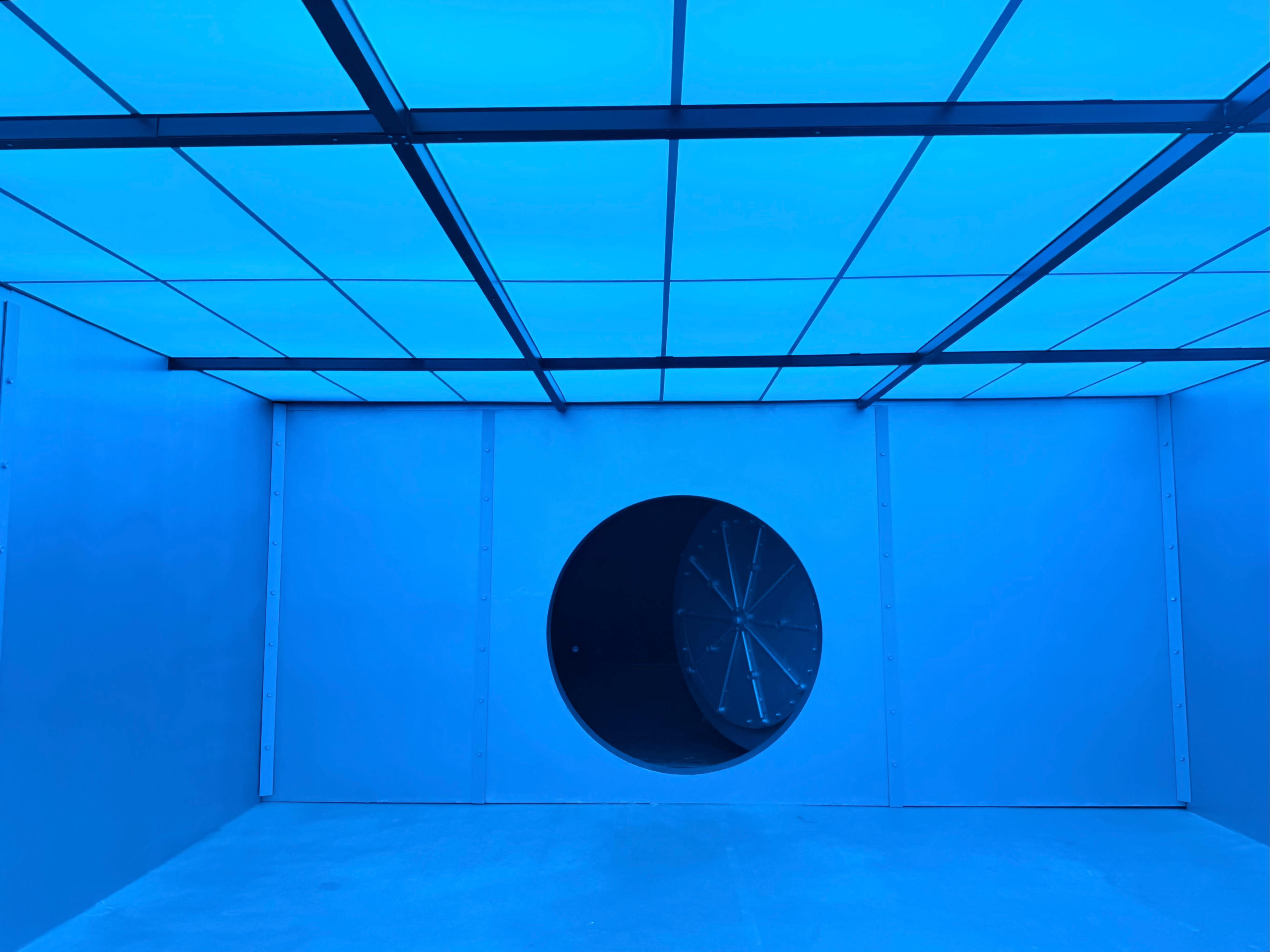 The image shows a minimalist room with blue walls and a large circular opening on one side.