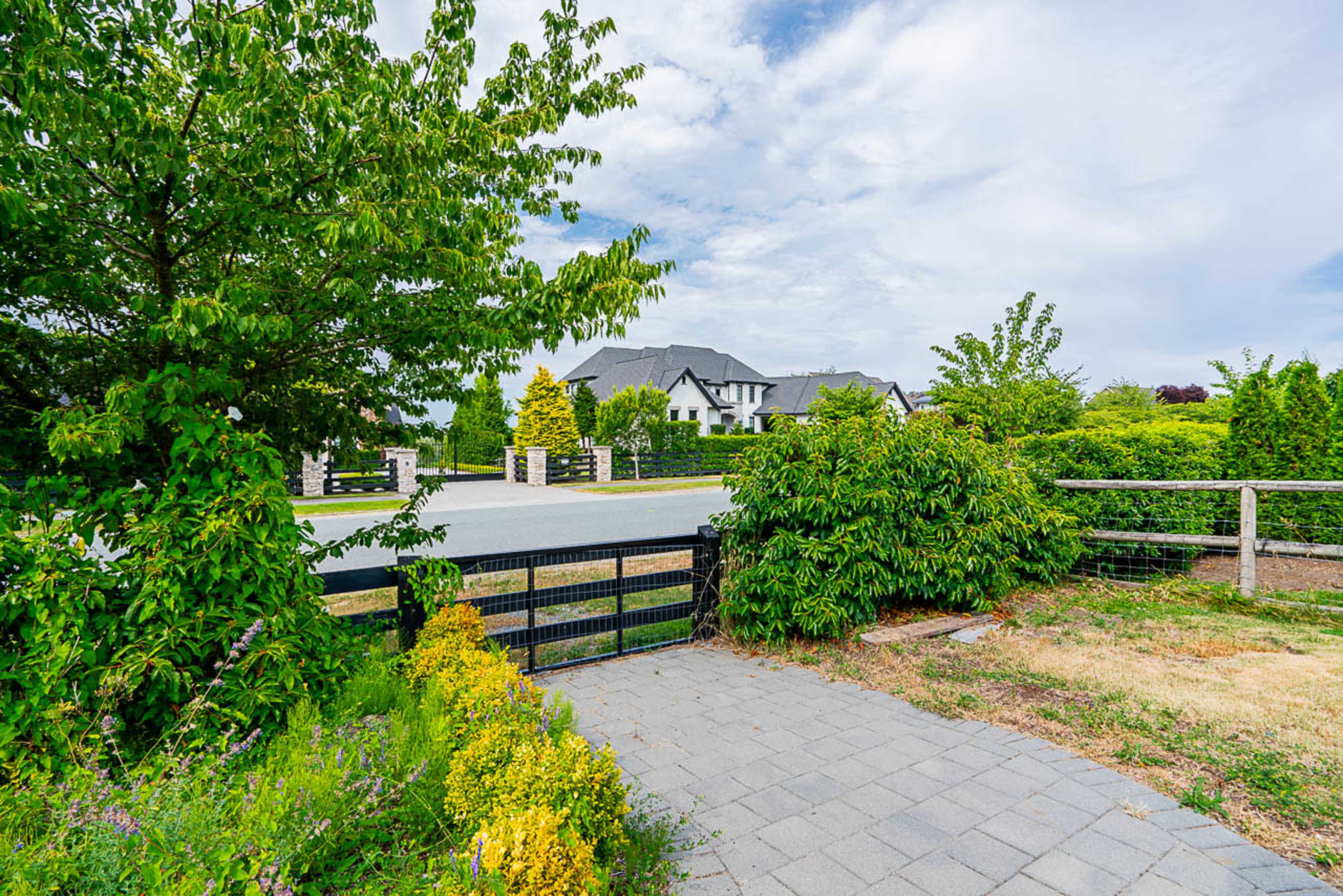 A landscaped pathway leading to a street lined with trees and a large house visible in the distance.