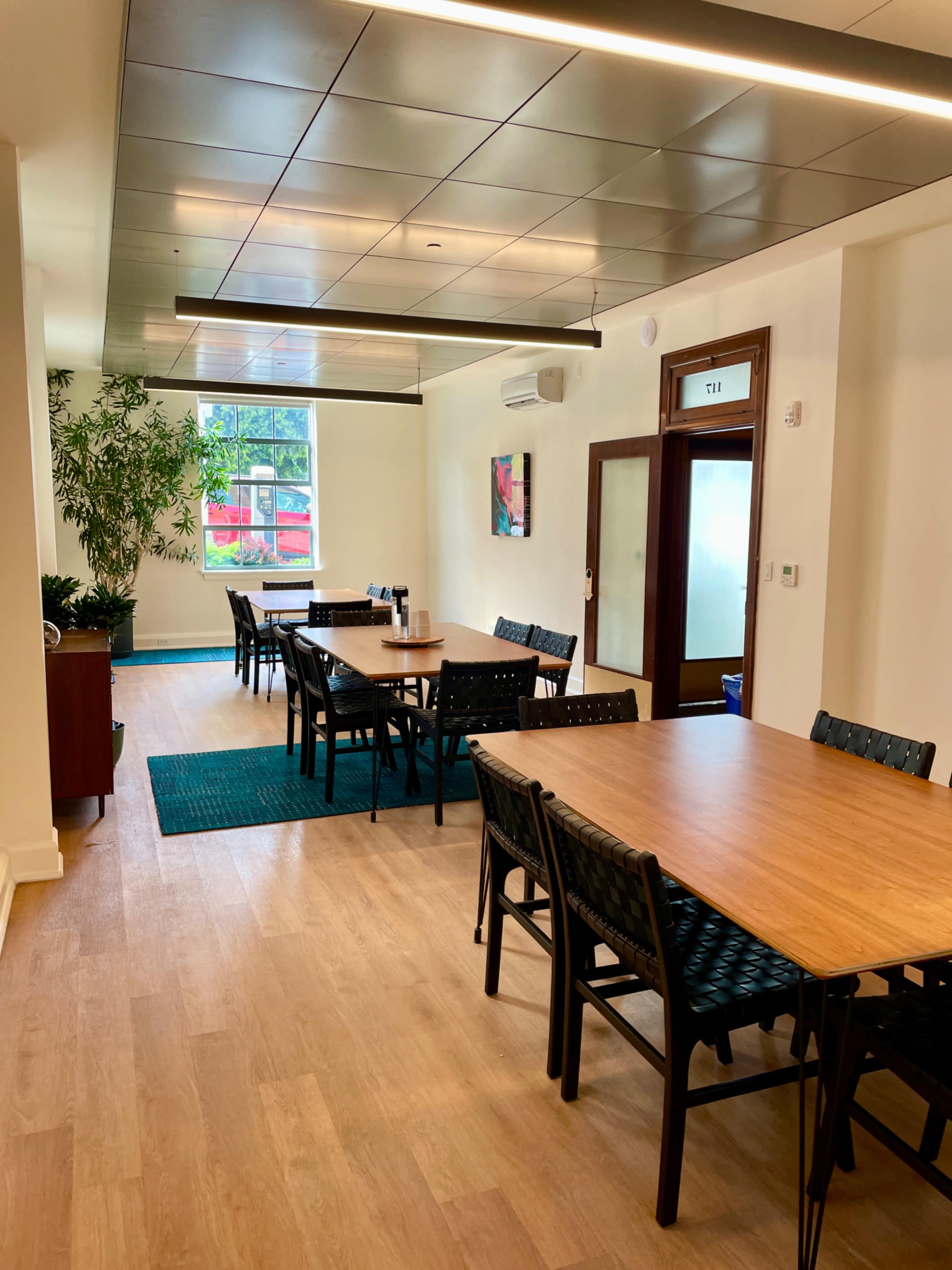 The image shows a well-arranged dining area with multiple wooden tables and chairs, illuminated by natural light from a window.