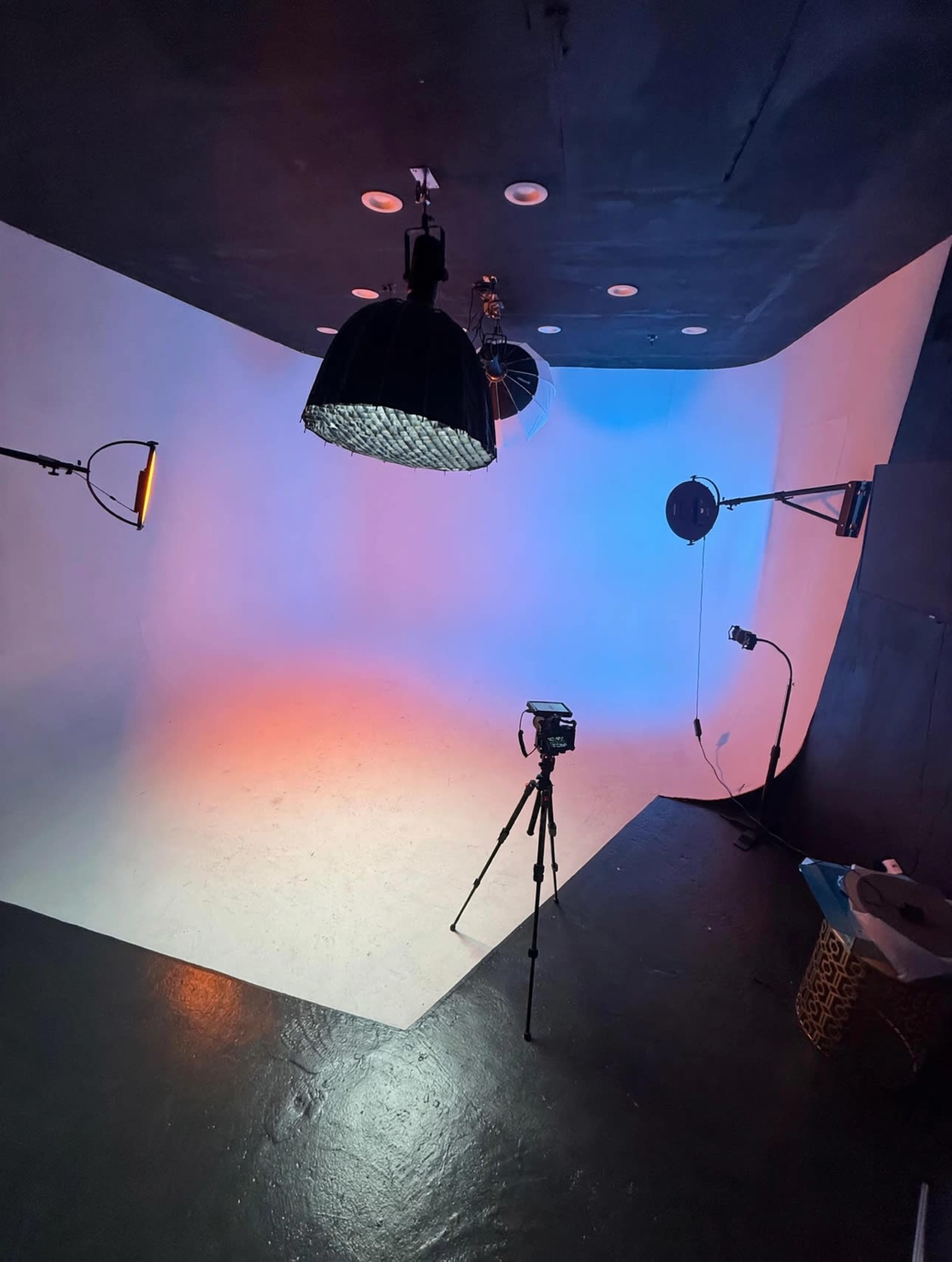 The image shows a photography studio with a gradient backdrop and various lighting equipment set up for a shoot.