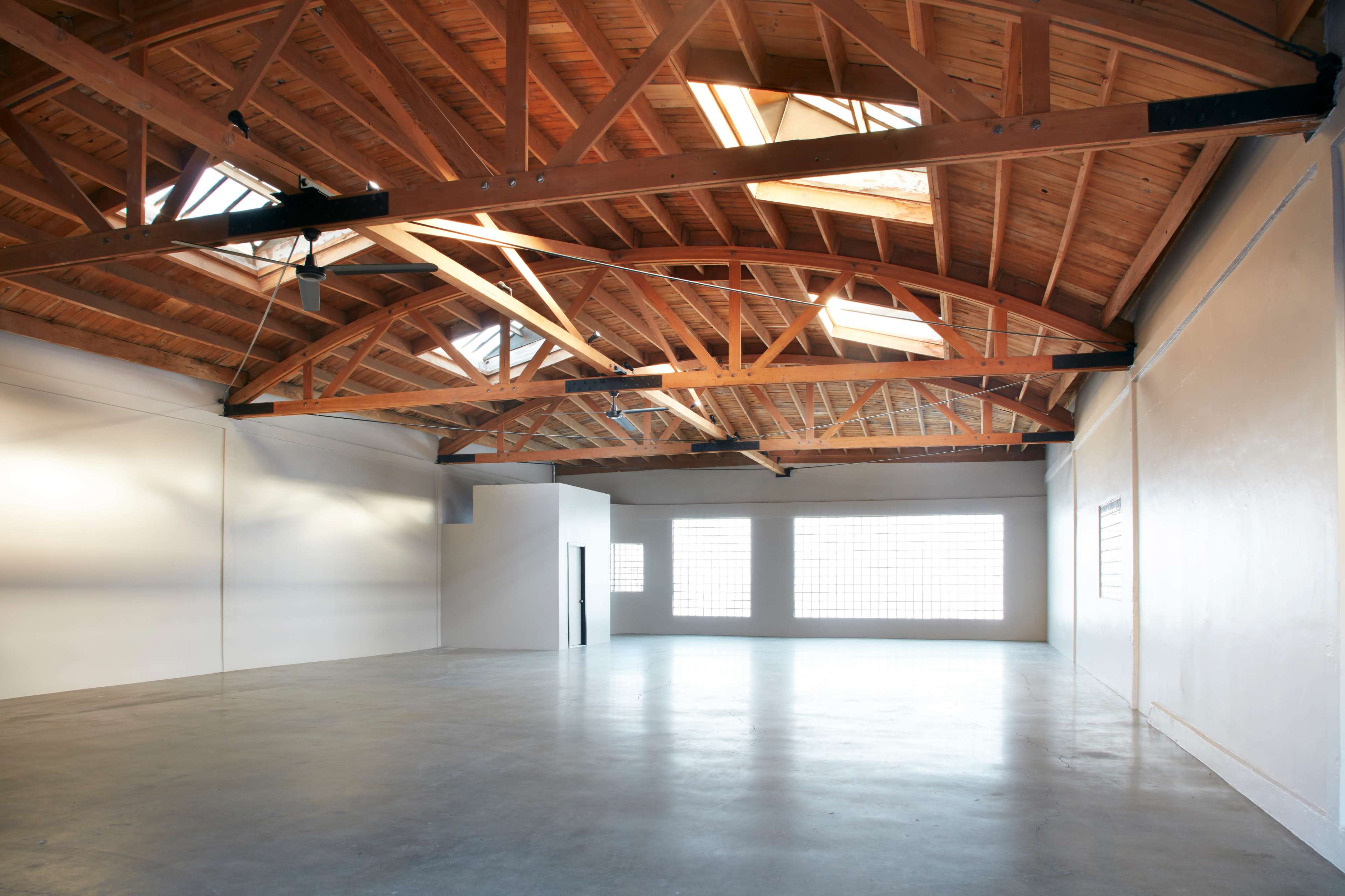 An empty industrial space features high wooden beams and large windows allowing natural light to fill the area.