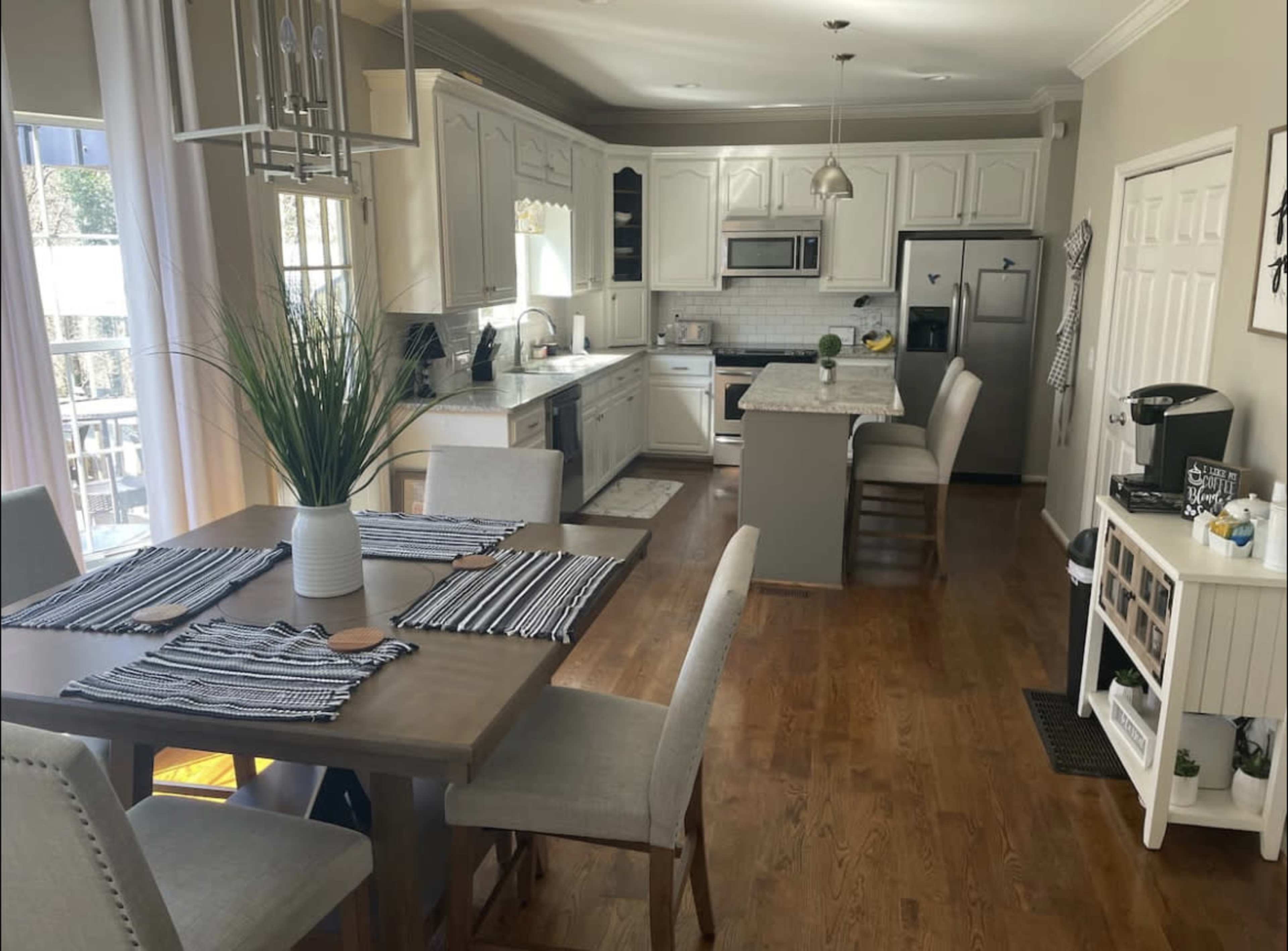 A modern kitchen and dining area with white cabinetry, a wooden table set for meals, and stainless steel appliances.
