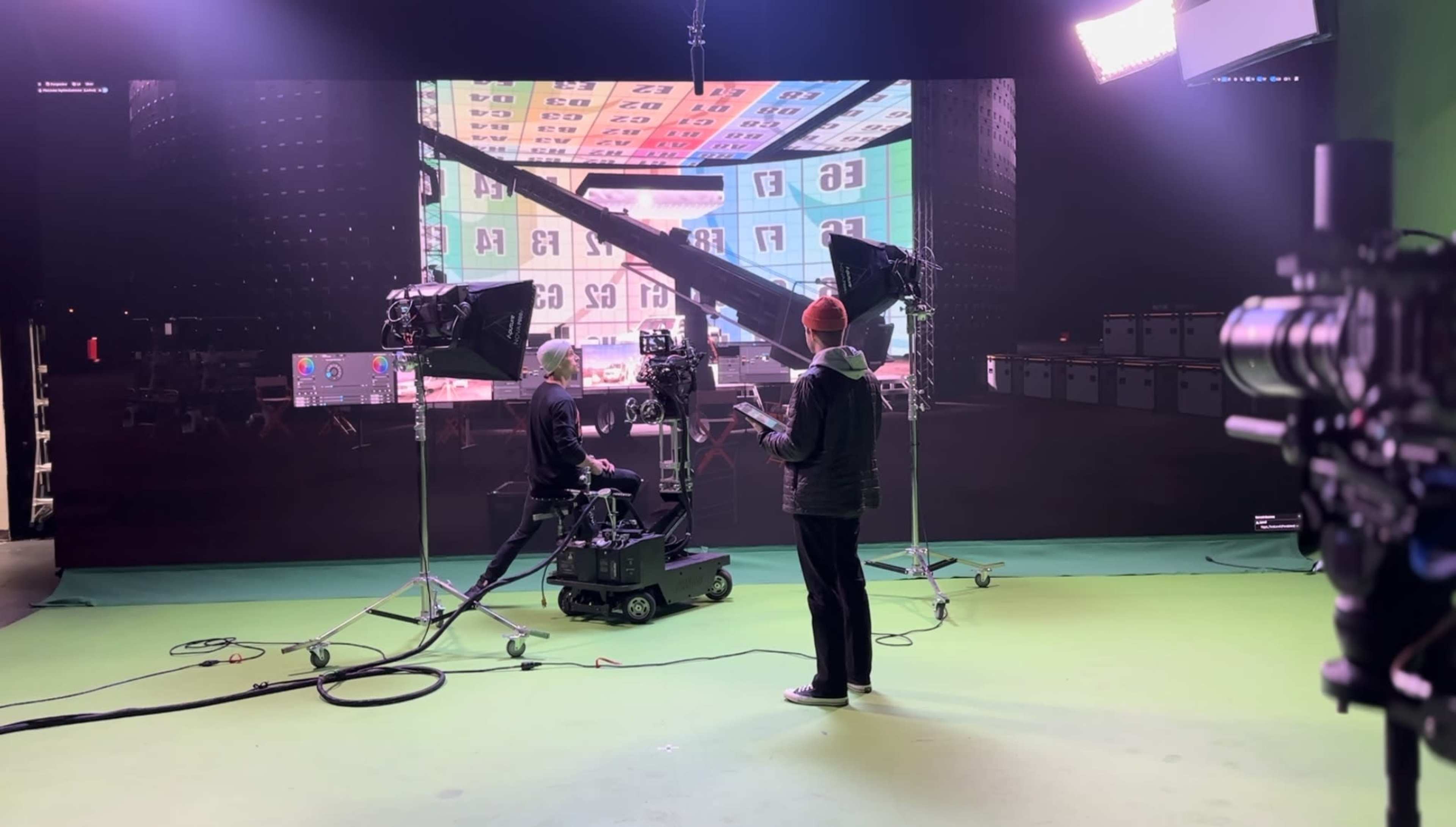A camera crew sets up a green screen studio with a large digital backdrop while one operator sits on a motorized dolly.