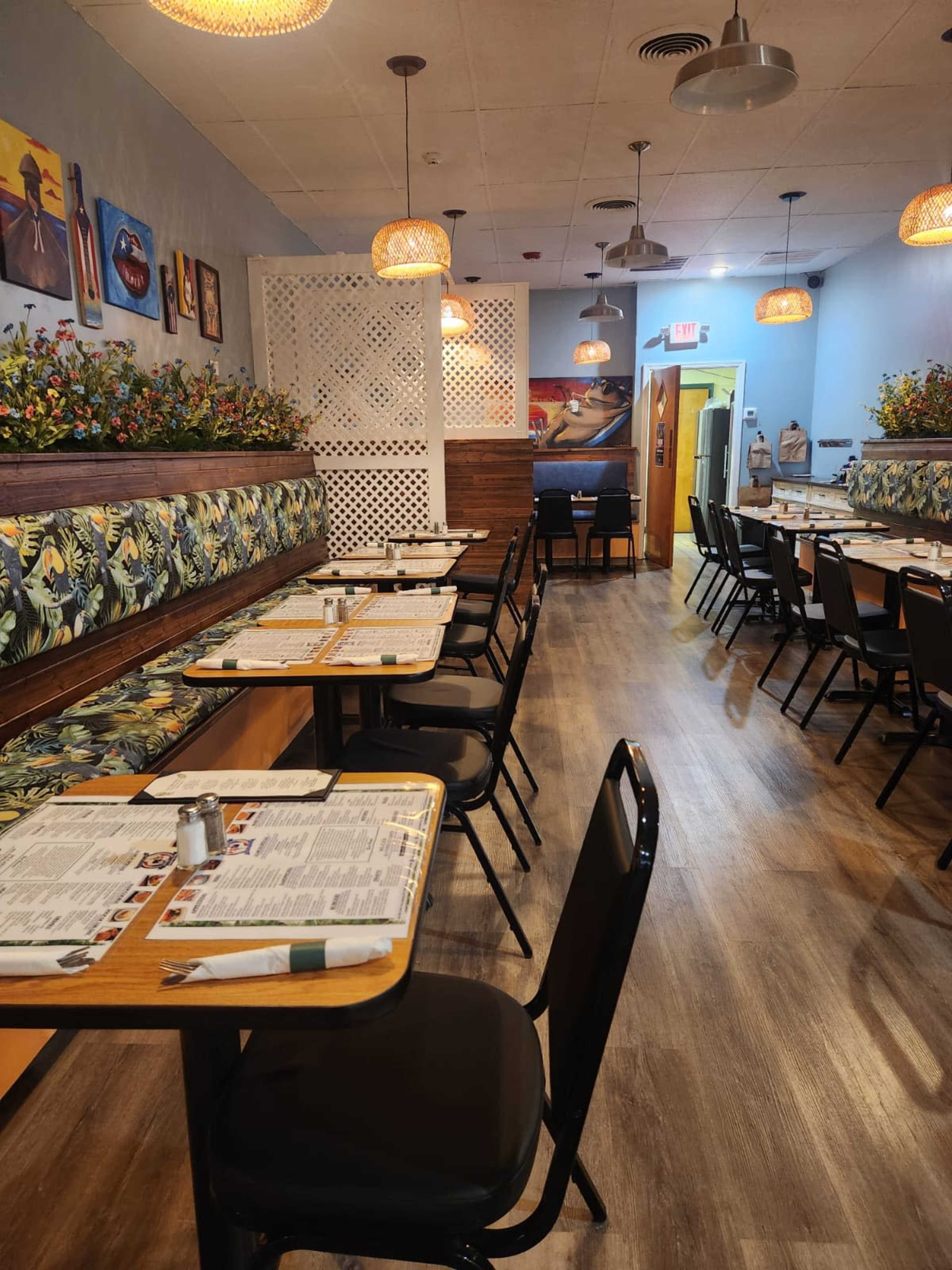 The image shows the interior of a restaurant featuring booths with floral decorations, wooden tables set with menus, and a layout of chairs aligned neatly along the dining area.