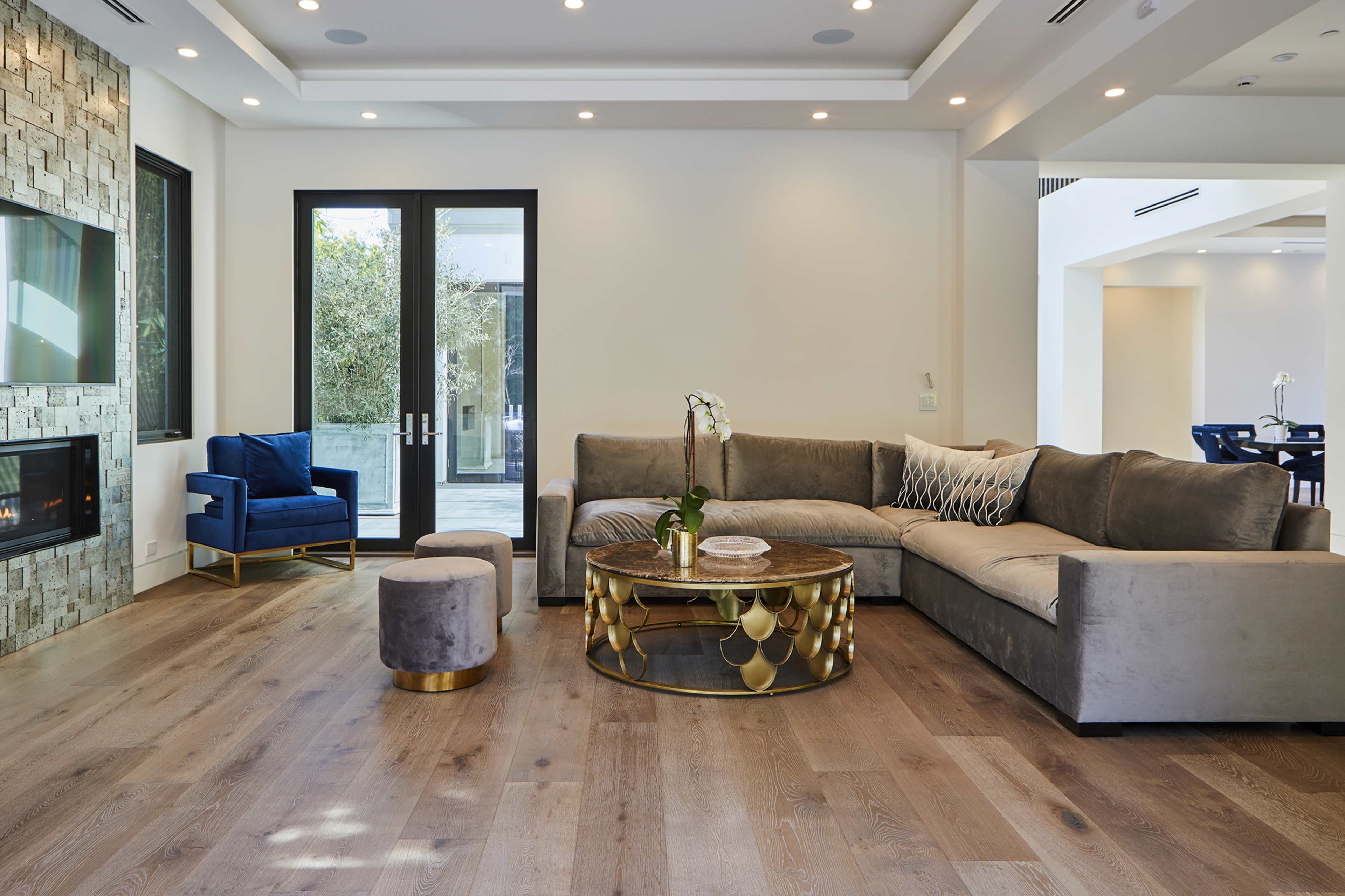 The living room features a sectional sofa, a round coffee table, and a blue armchair, with large windows providing natural light.