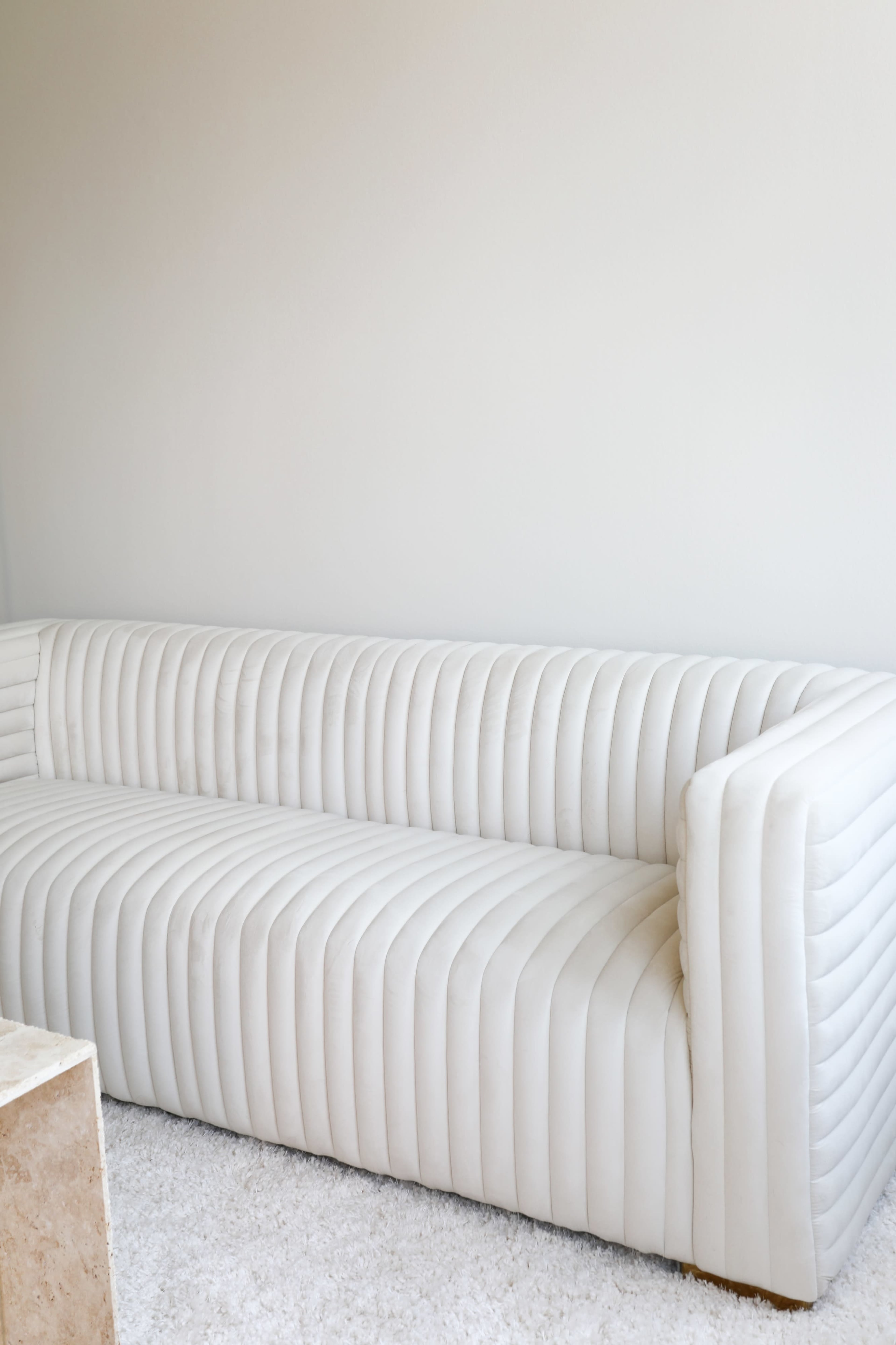 A white, ribbed sofa is positioned against a plain wall in a softly lit room.