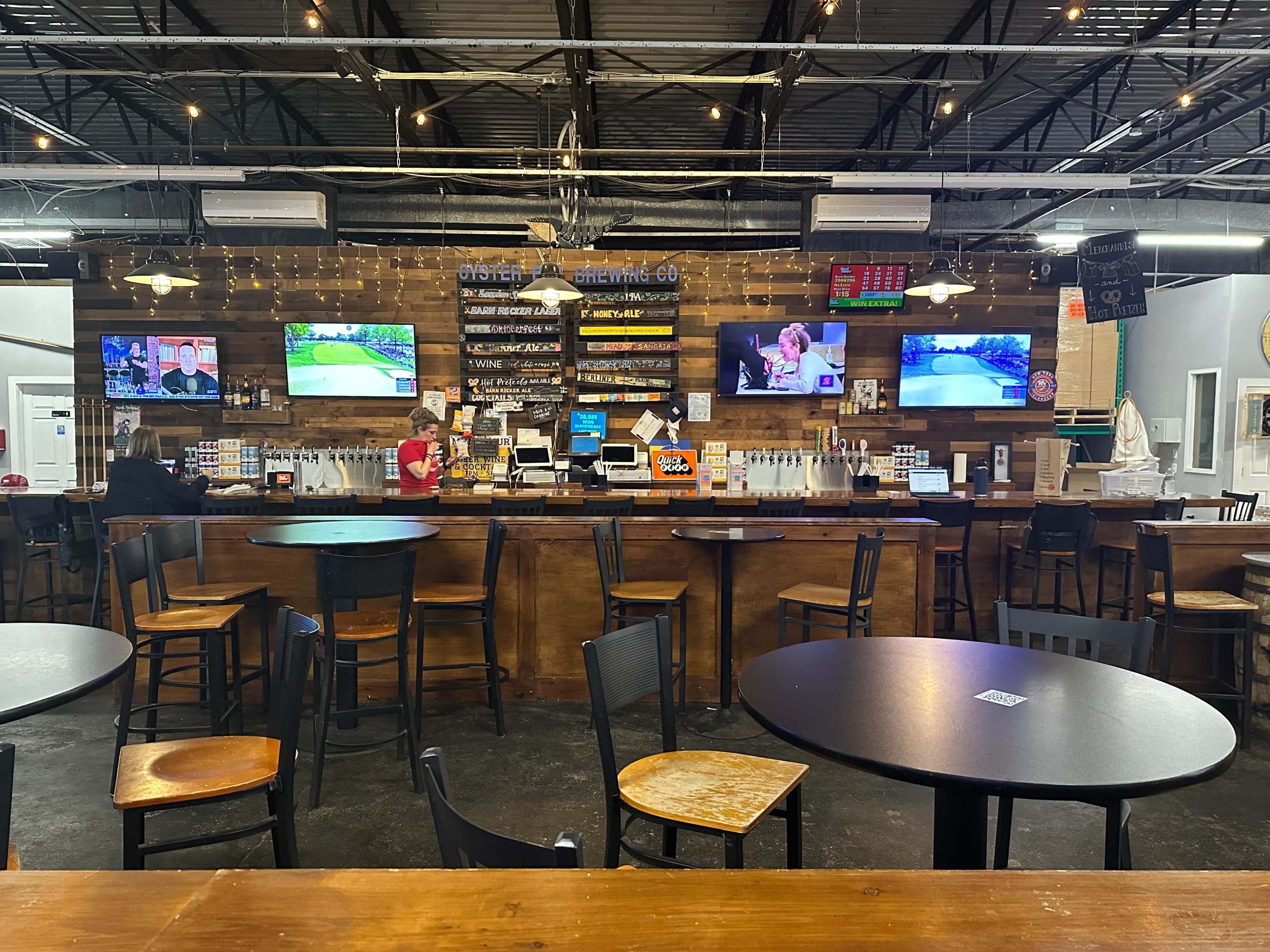 The image shows a bar area with wooden tables and chairs, a counter with various drinks, and multiple screens displaying sports events.