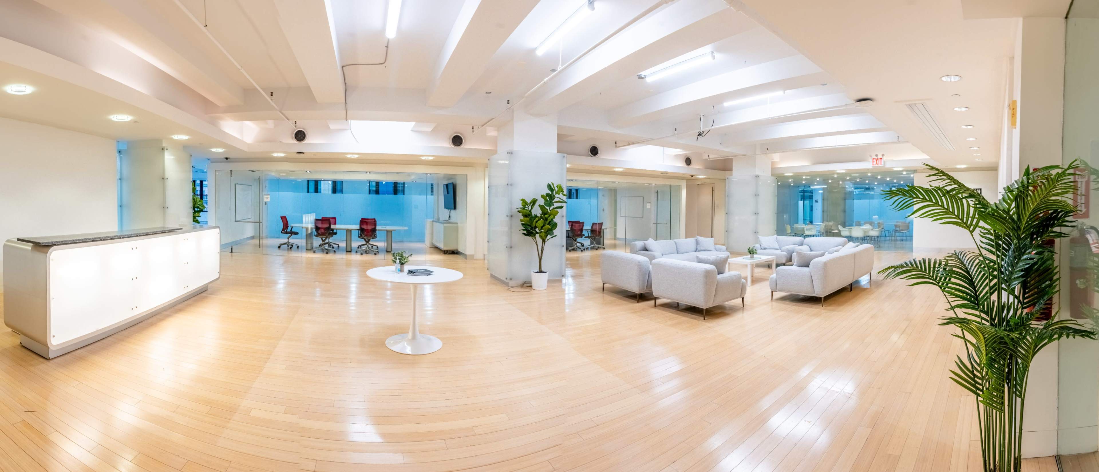 The image shows a modern, open office space with seating areas, conference rooms, and natural light from large windows.