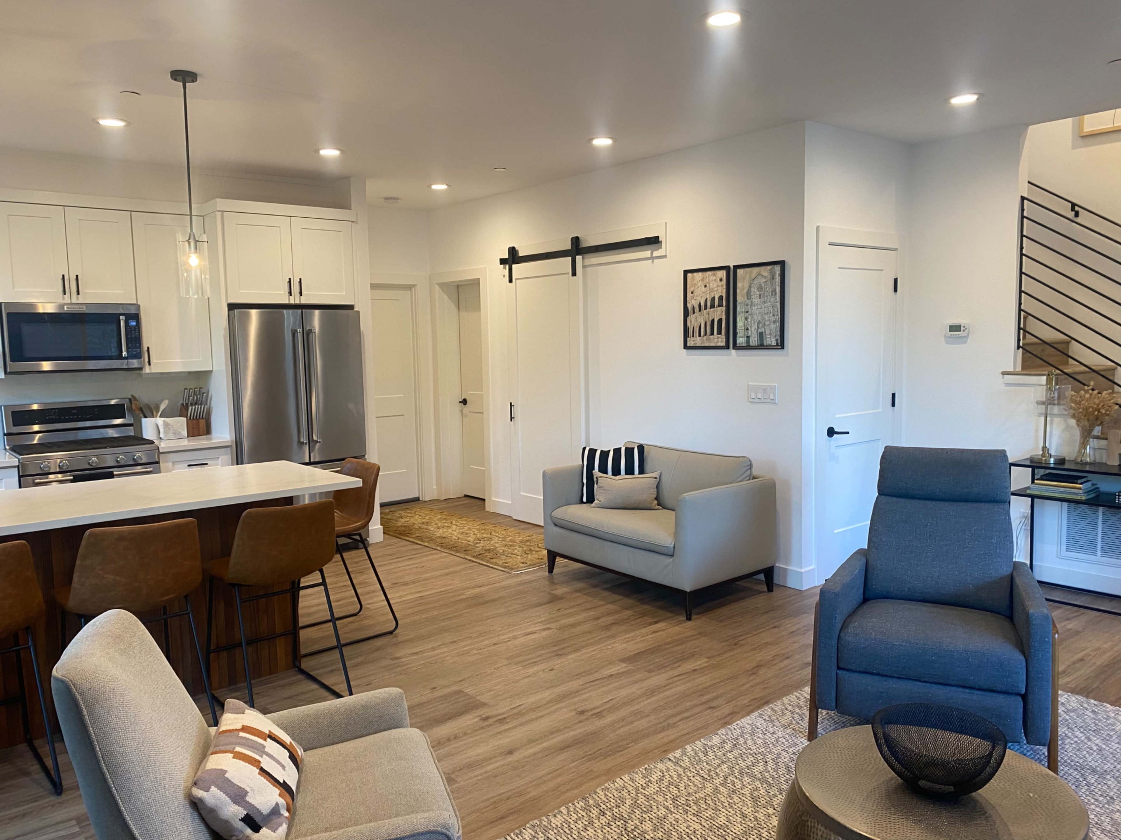 A modern open-concept living space with a kitchen, dining area, and seating arrangements featuring two armchairs and a couch.