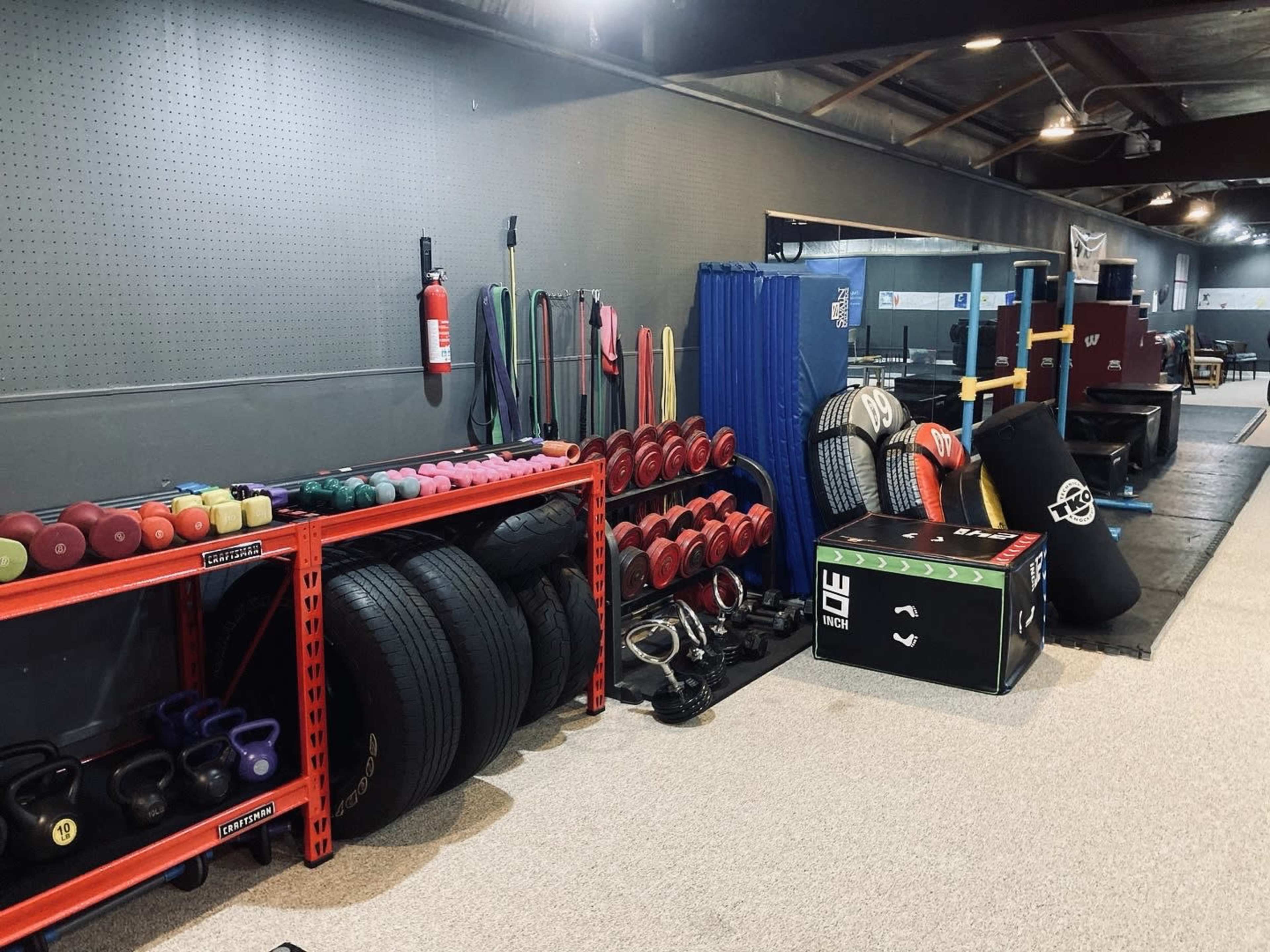 A gym storage area with various weights, exercise equipment, and colorful resistance bands organized on a rack.