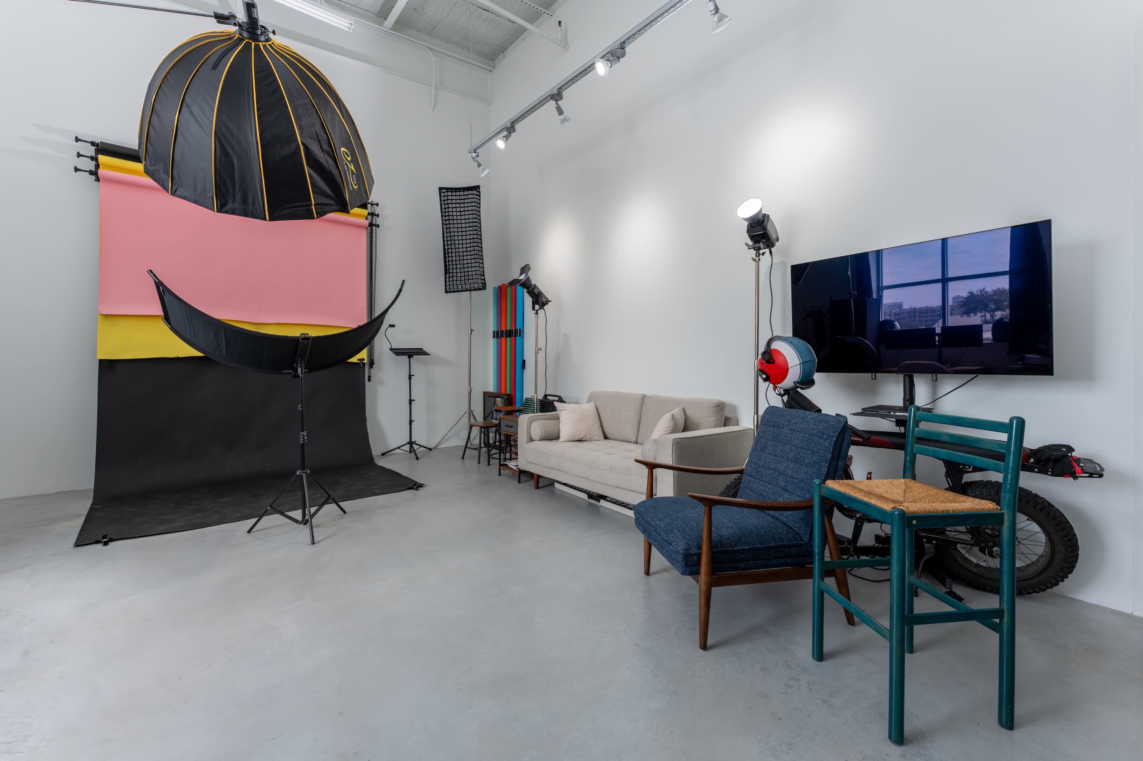 The image shows a photography studio with a colorful backdrop, a couch, chairs, and various lighting equipment.