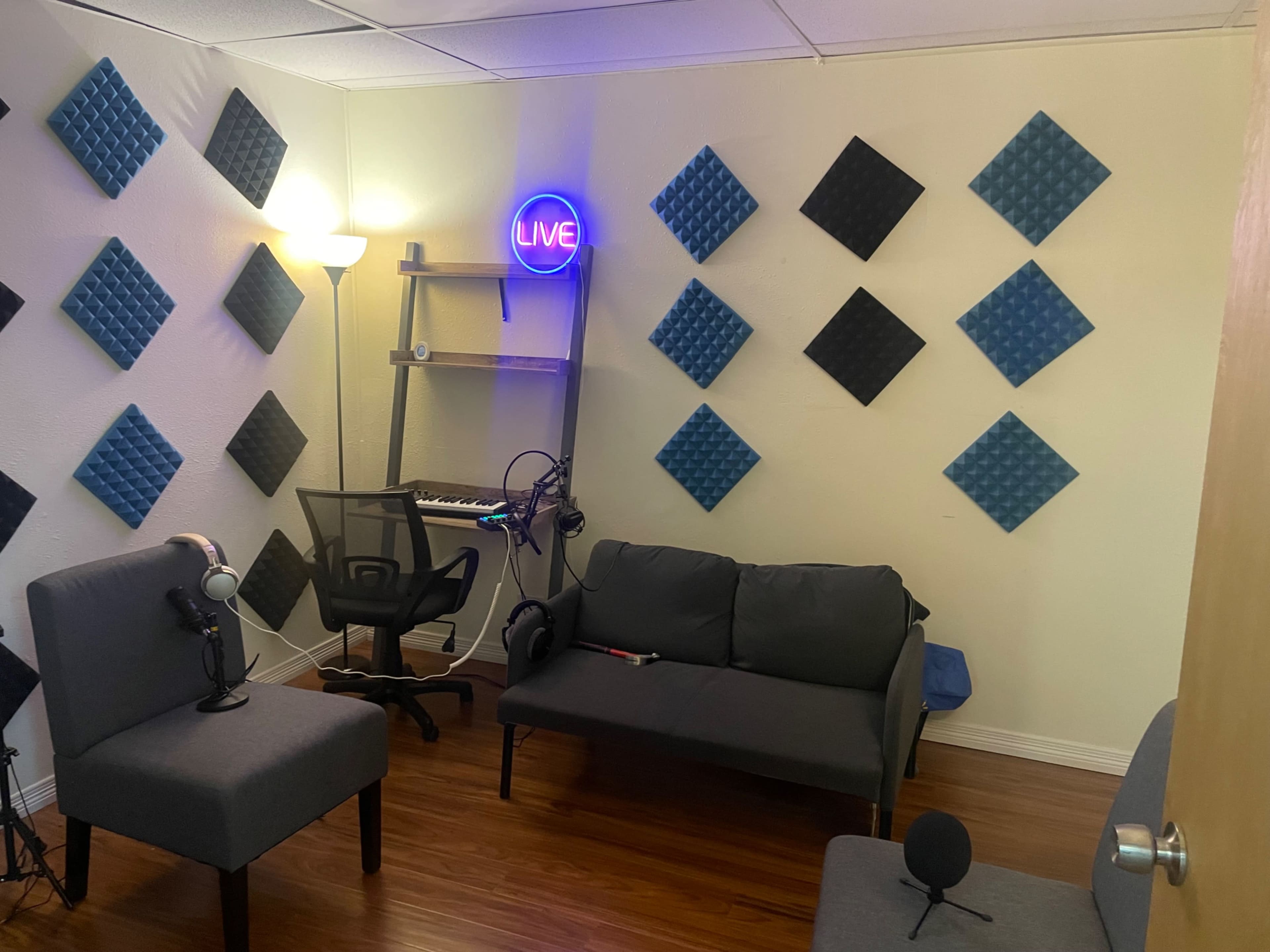 The image shows a small recording studio with soundproof panels on the walls, a keyboard, and seating arrangements for recording or broadcasting.