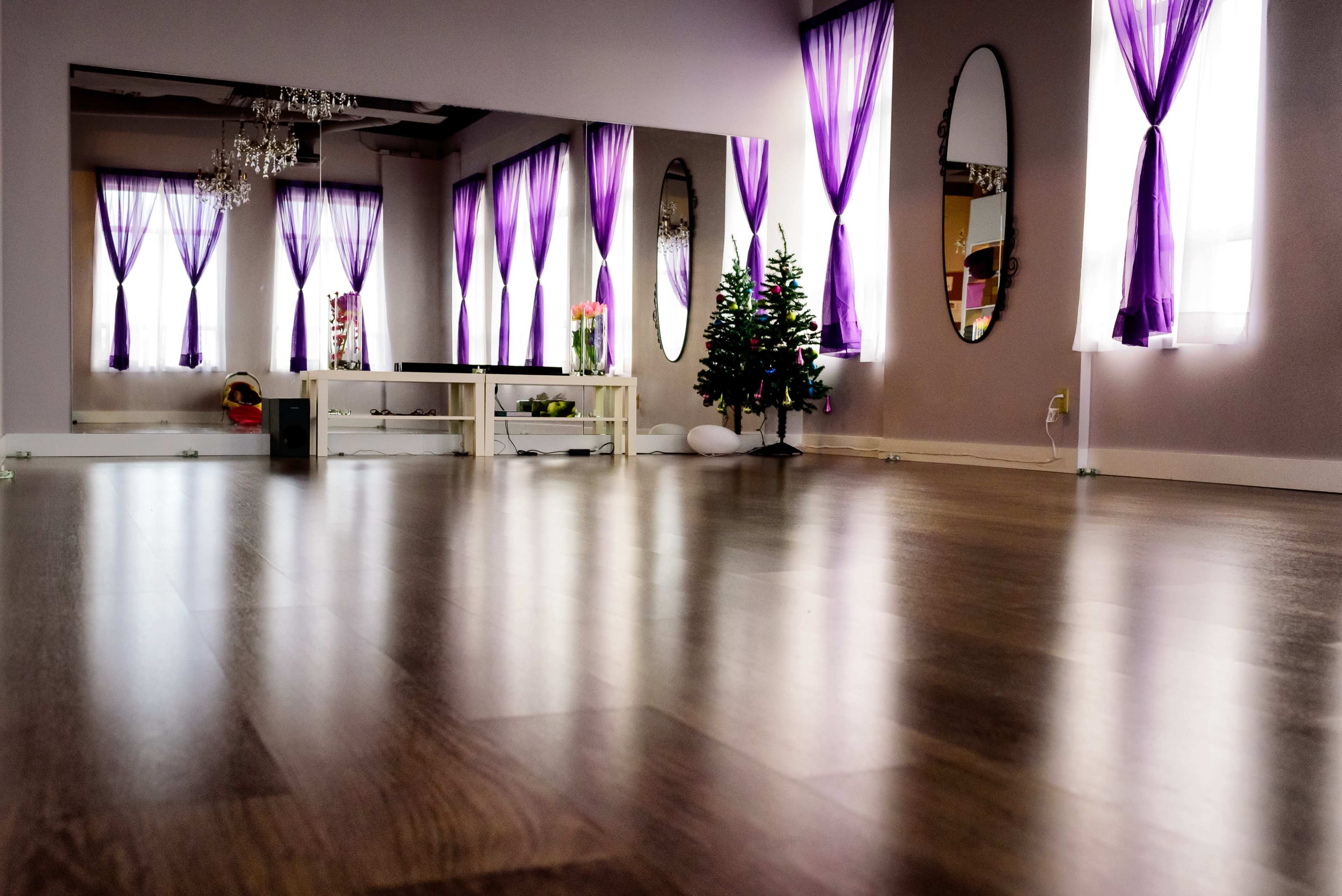 A spacious room with wooden flooring, large mirrors, and purple curtains, featuring a small Christmas tree in one corner.