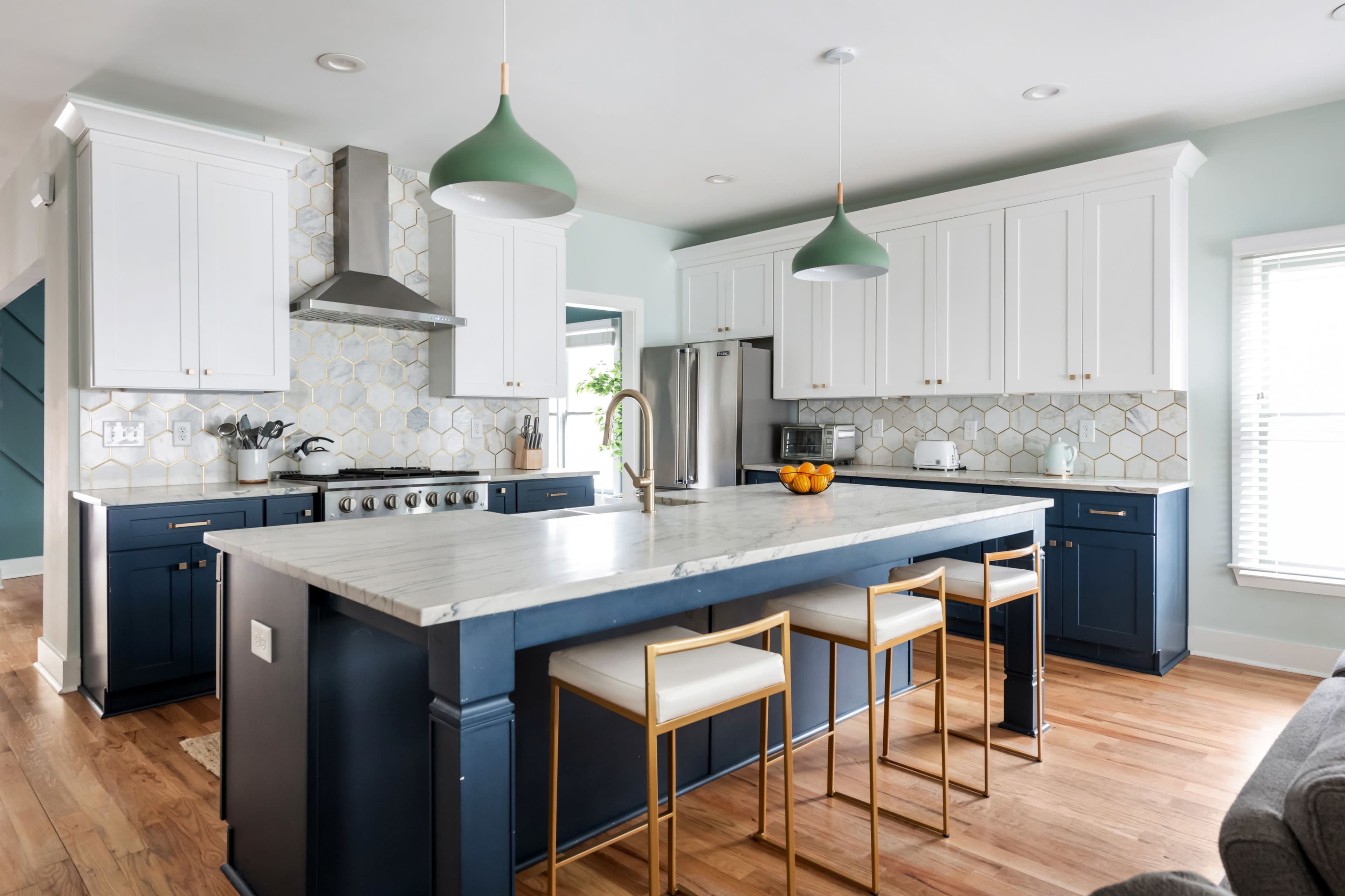 The kitchen features a central island with bar seating, blue cabinetry, white upper cabinets, and a marble countertop.