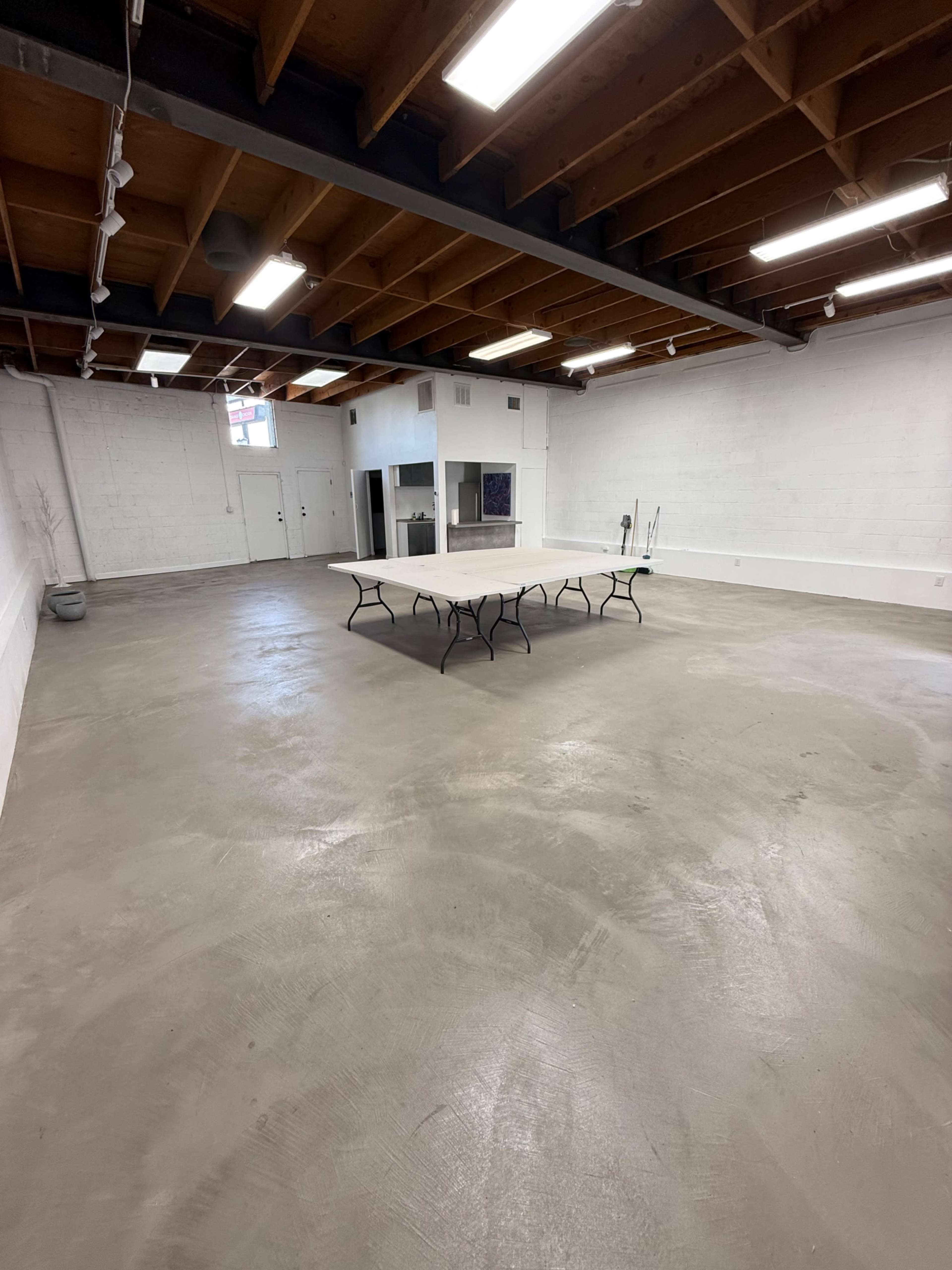An empty room with a concrete floor and a folding table positioned in the center under ceiling lights.