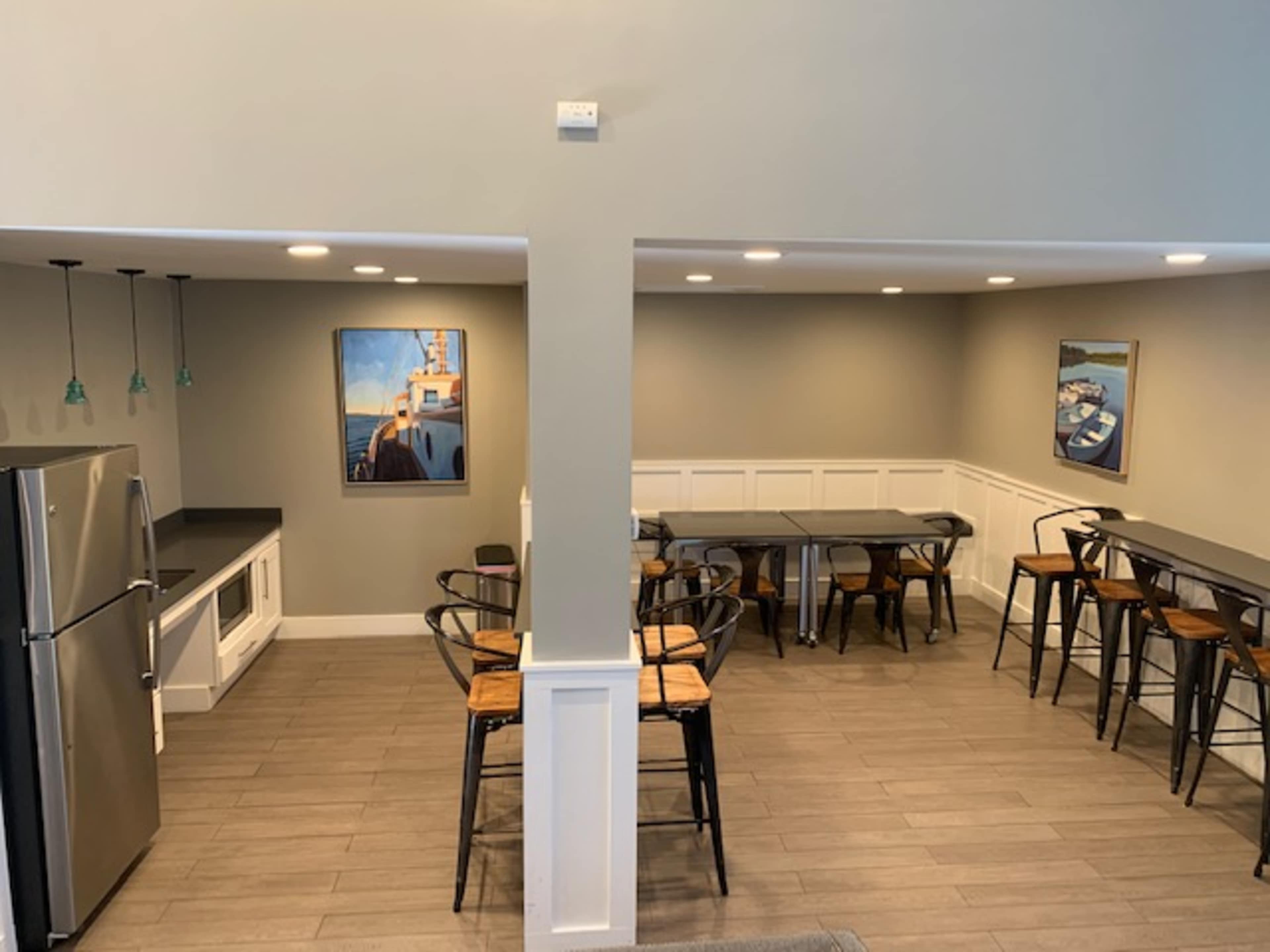 A spacious kitchen and dining area featuring stainless steel appliances, bar stools, and tables against a neutral wall with framed artwork.
