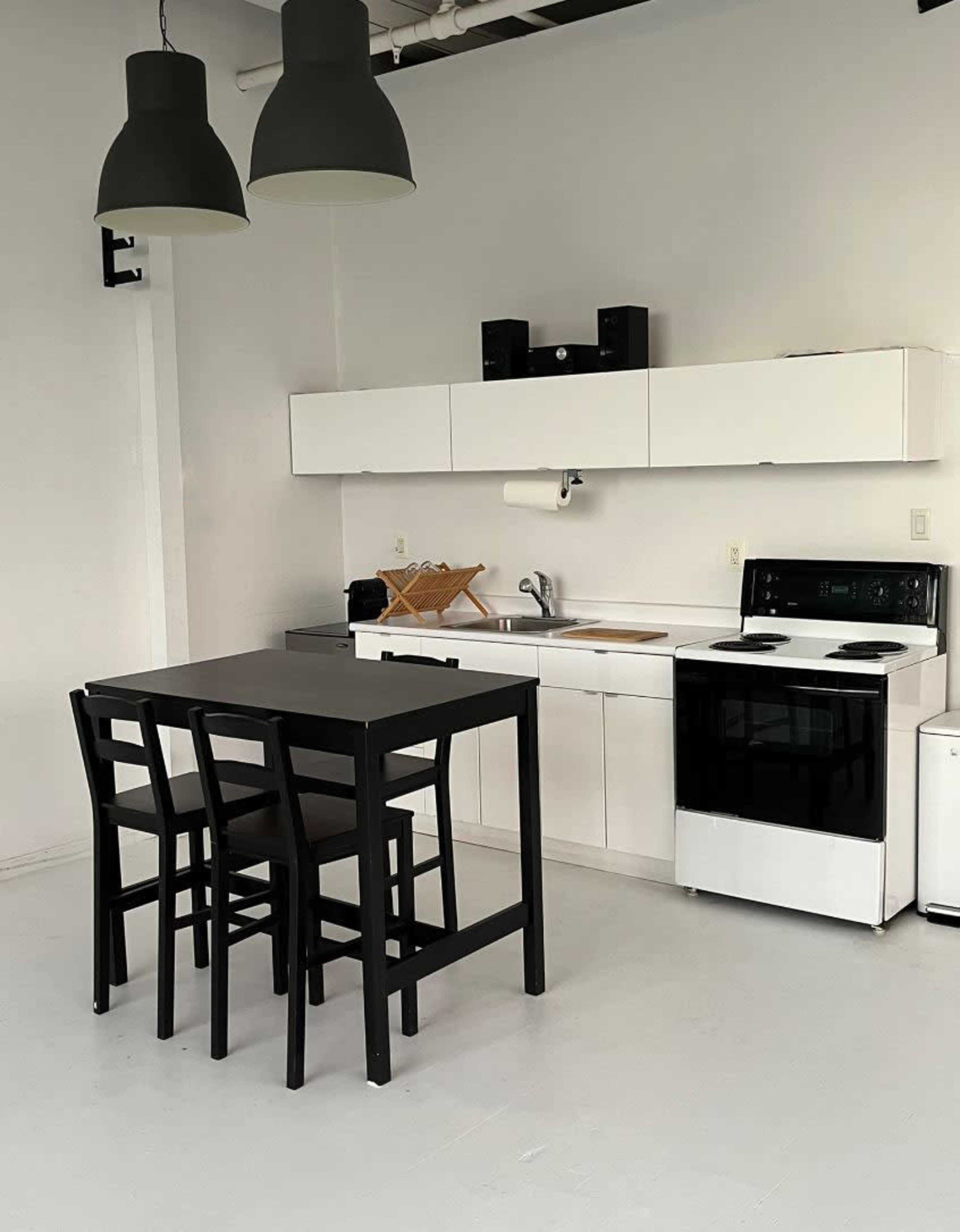 A minimalist kitchen with a white cabinetry, black appliances, and a black dining table with three high-backed chairs.