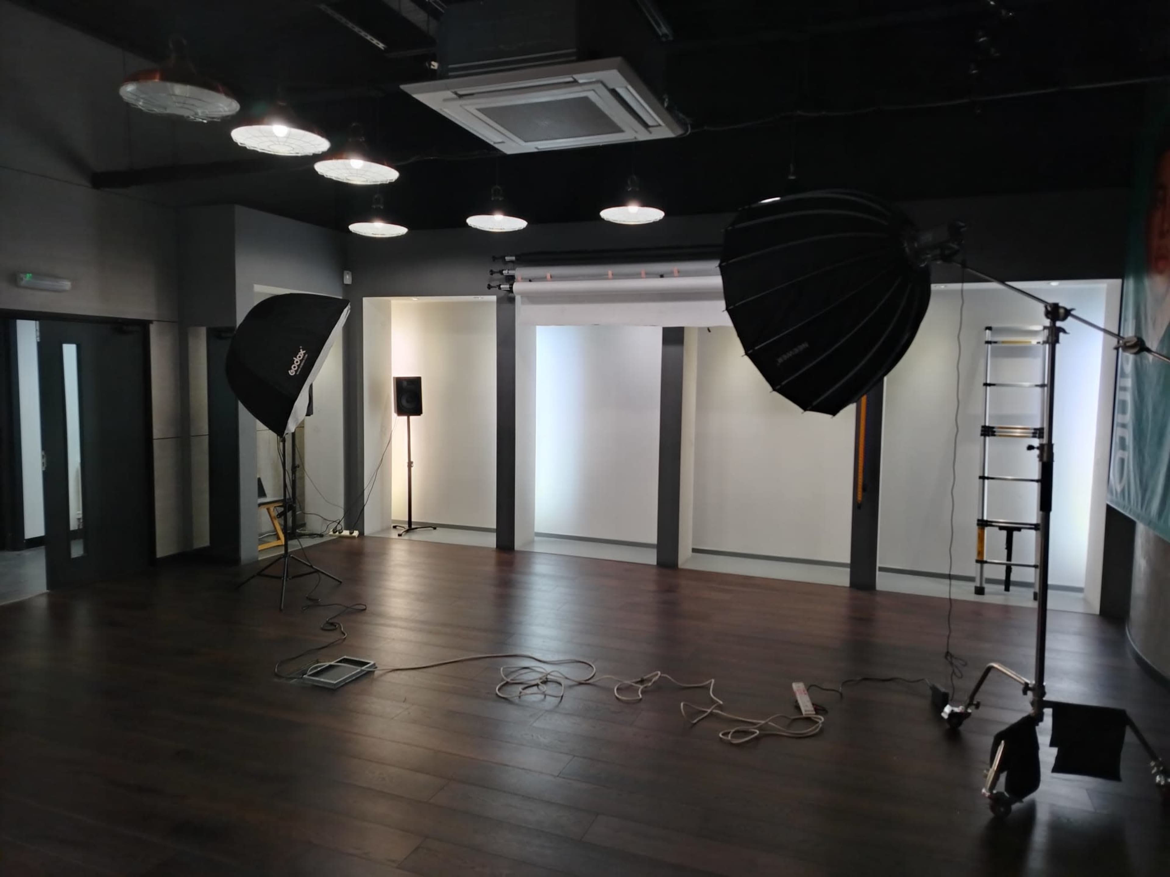 The image shows a photography studio with two large light modifiers, a ladder, and a backdrop set up against plain white walls.