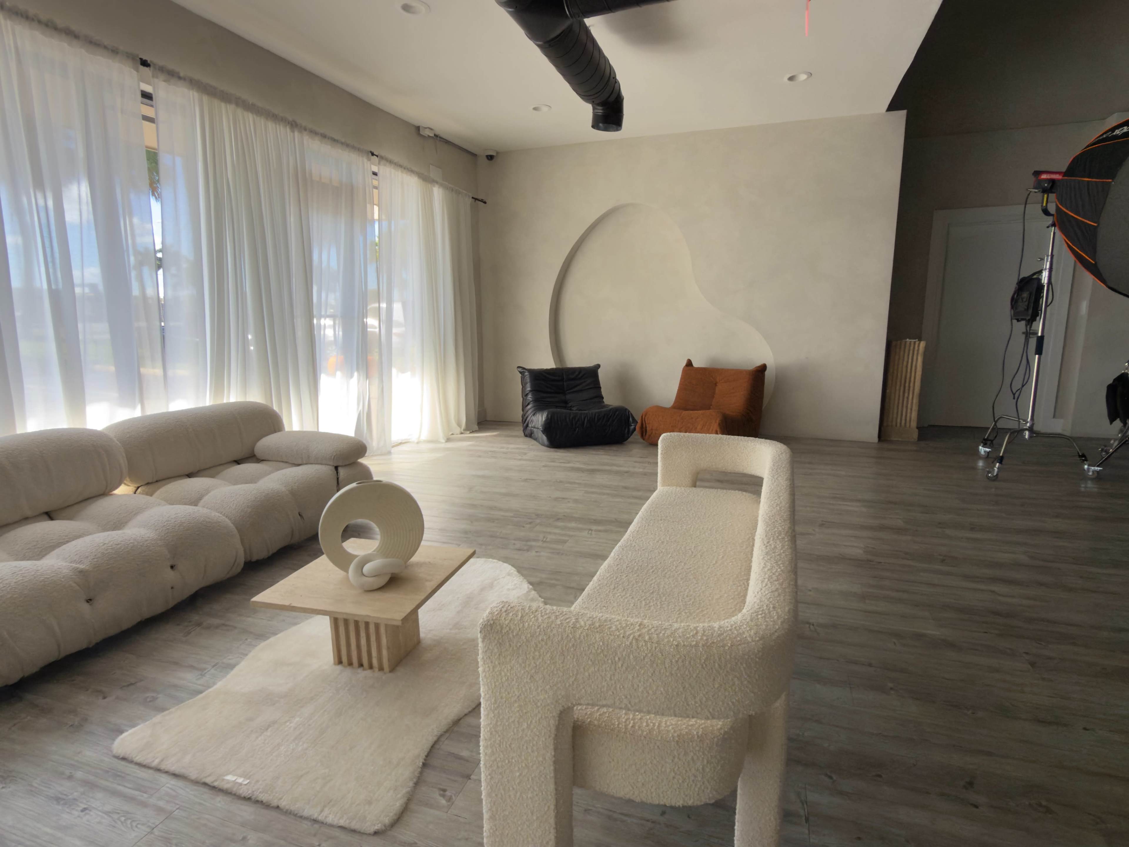 The image shows a modern interior space with a light-colored sofa, a coffee table, and a textured wall featuring a unique curved indentation, complemented by a soft carpet and large windows.