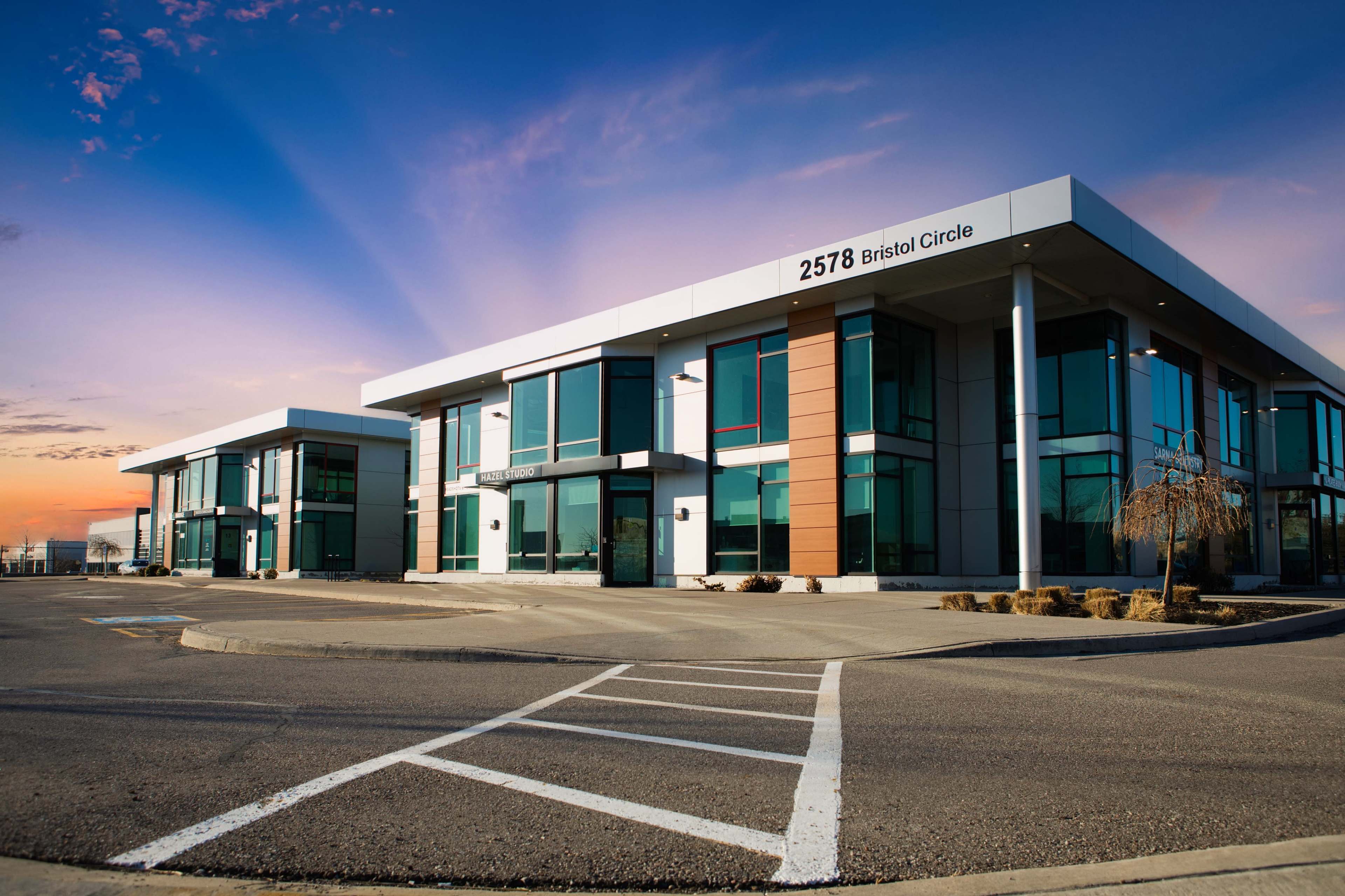 The image shows a modern office building with large windows and a clear sky at sunset.