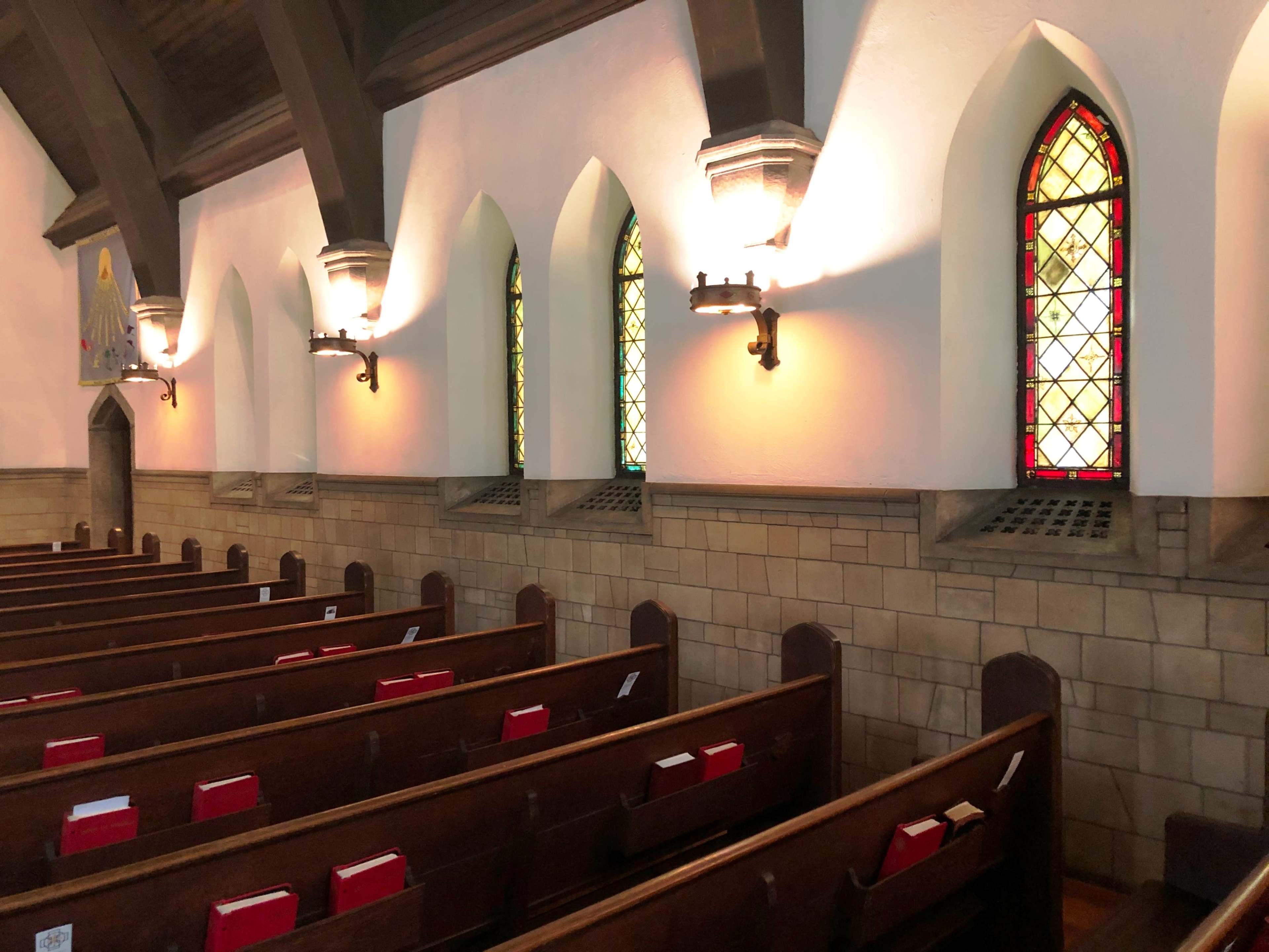The image shows the interior of a church with wooden pews and stained glass windows along the walls.