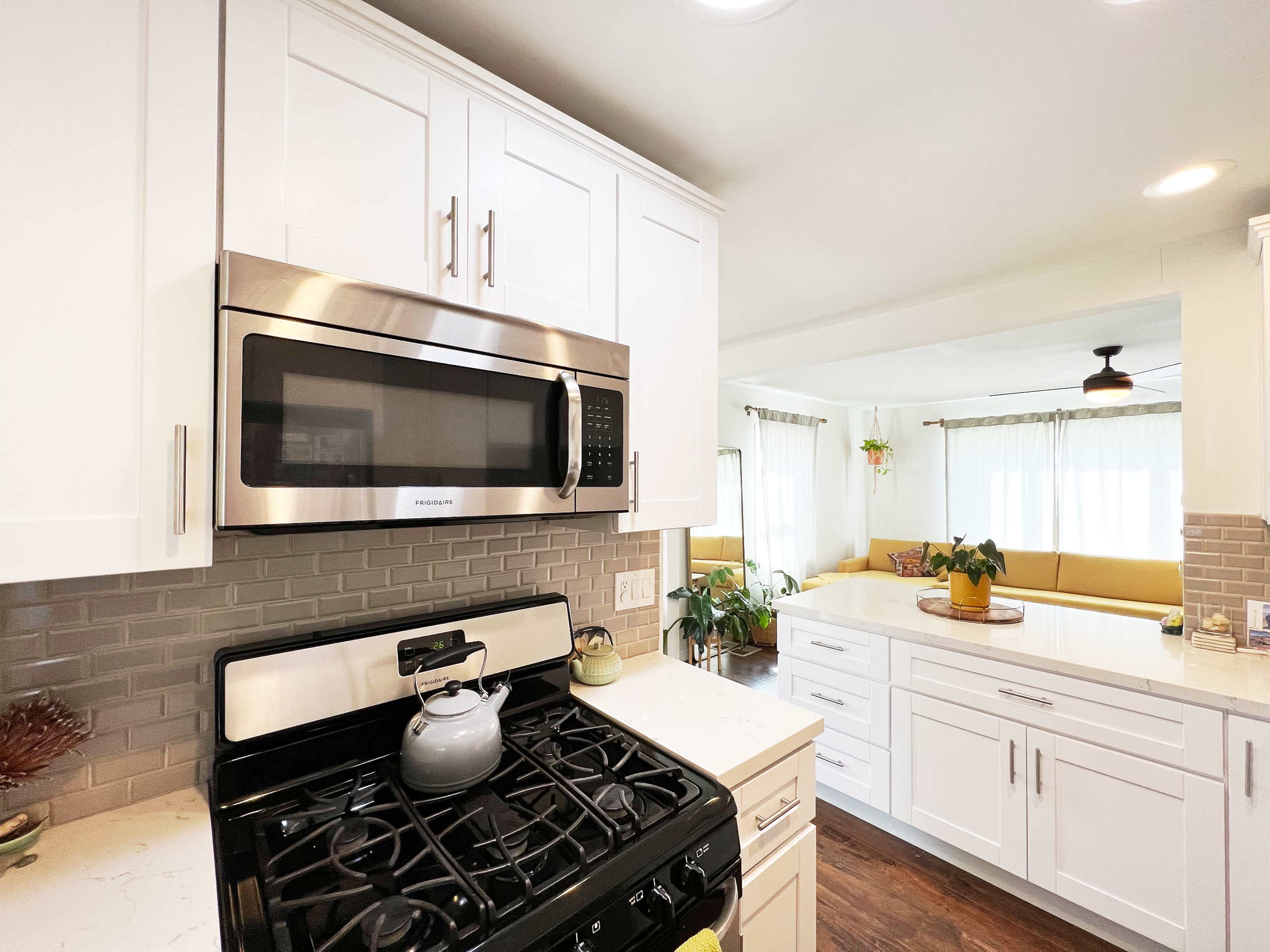 A modern kitchen featuring white cabinetry, stainless steel appliances, and a view into a bright living area with a yellow sectional sofa.