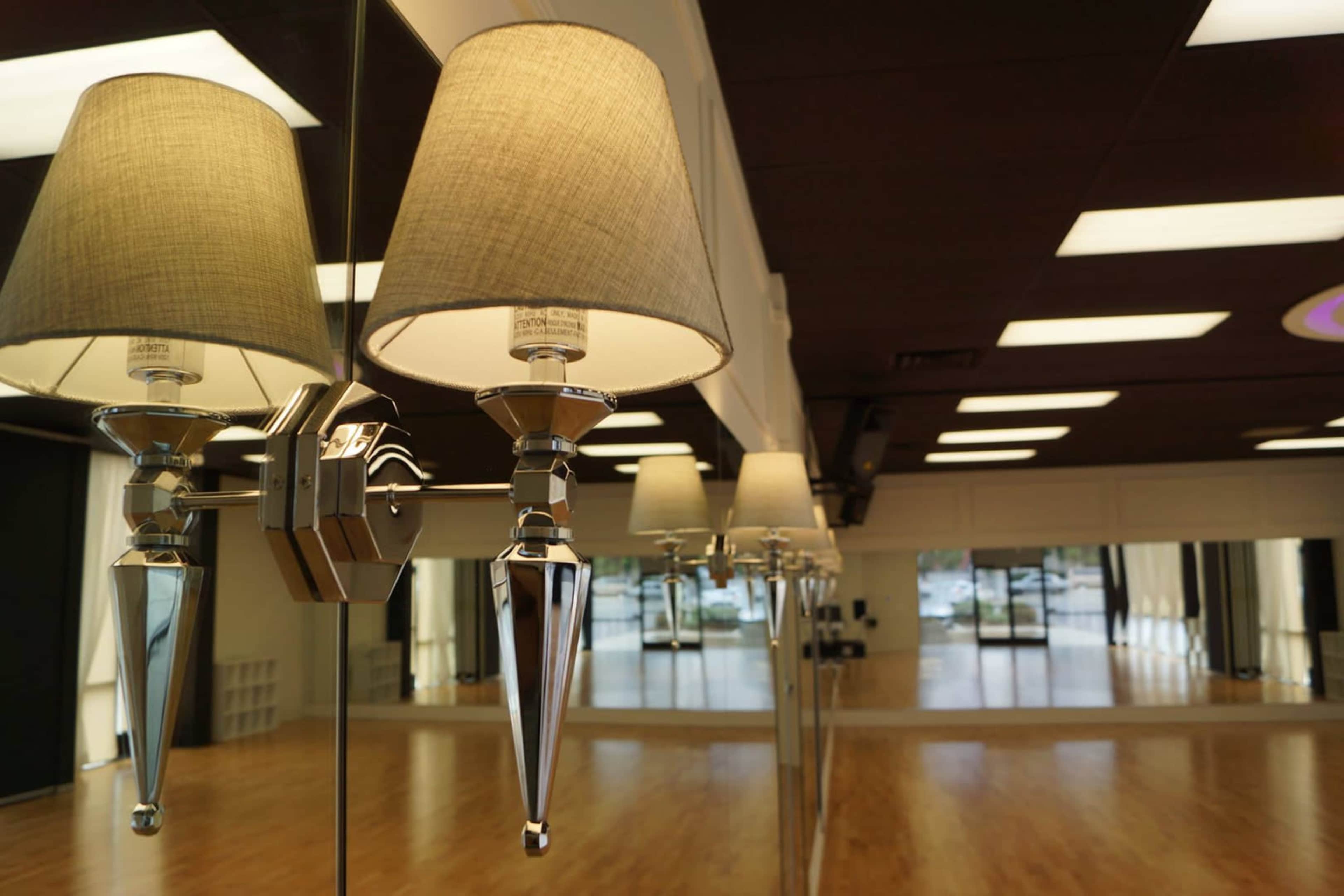 A wall-mounted lamp with a fabric shade reflecting on a glass surface in a spacious, well-lit studio.