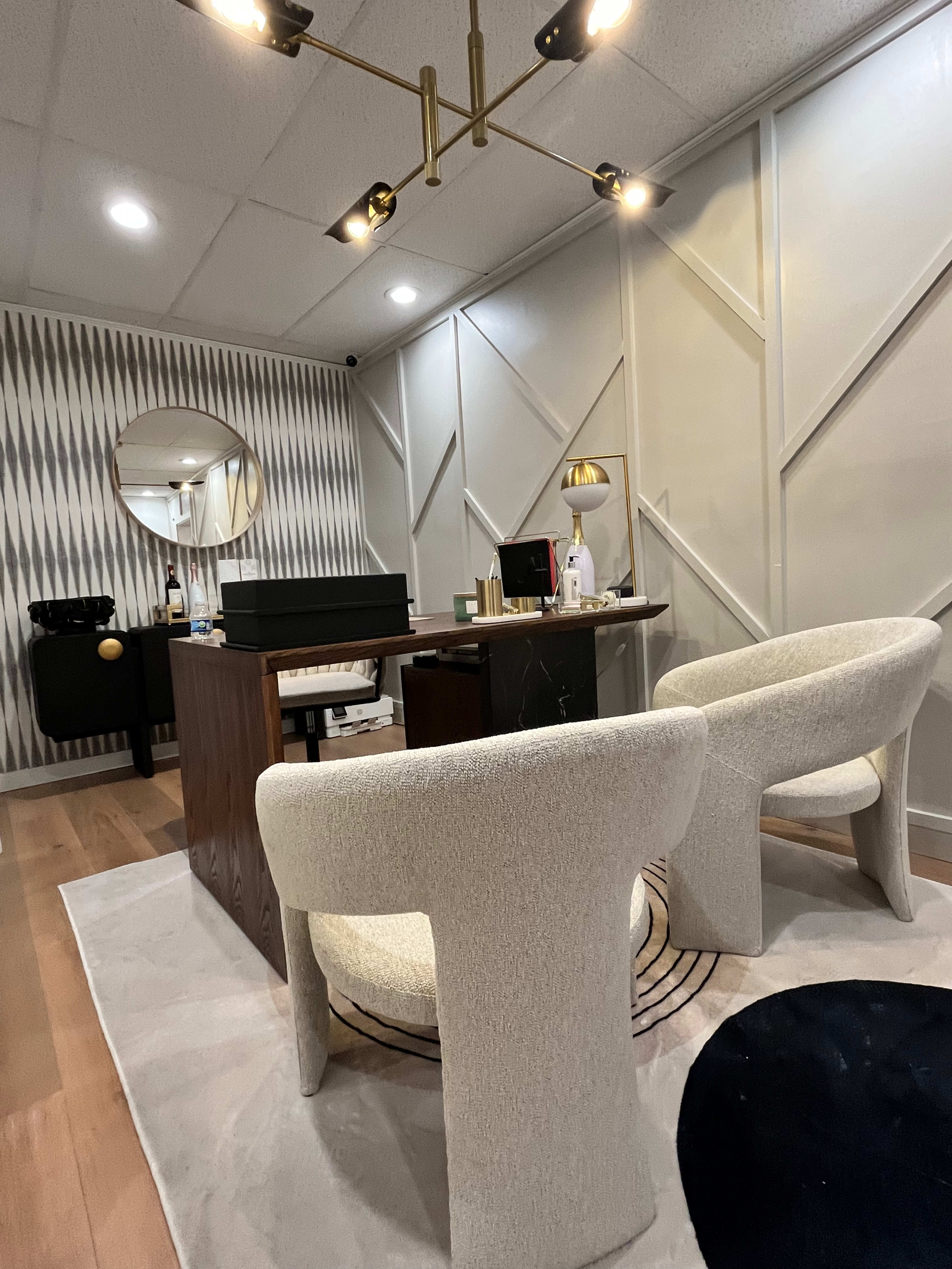 A modern office space featuring a wooden desk, two upholstered chairs, and wall decor with geometric patterns.