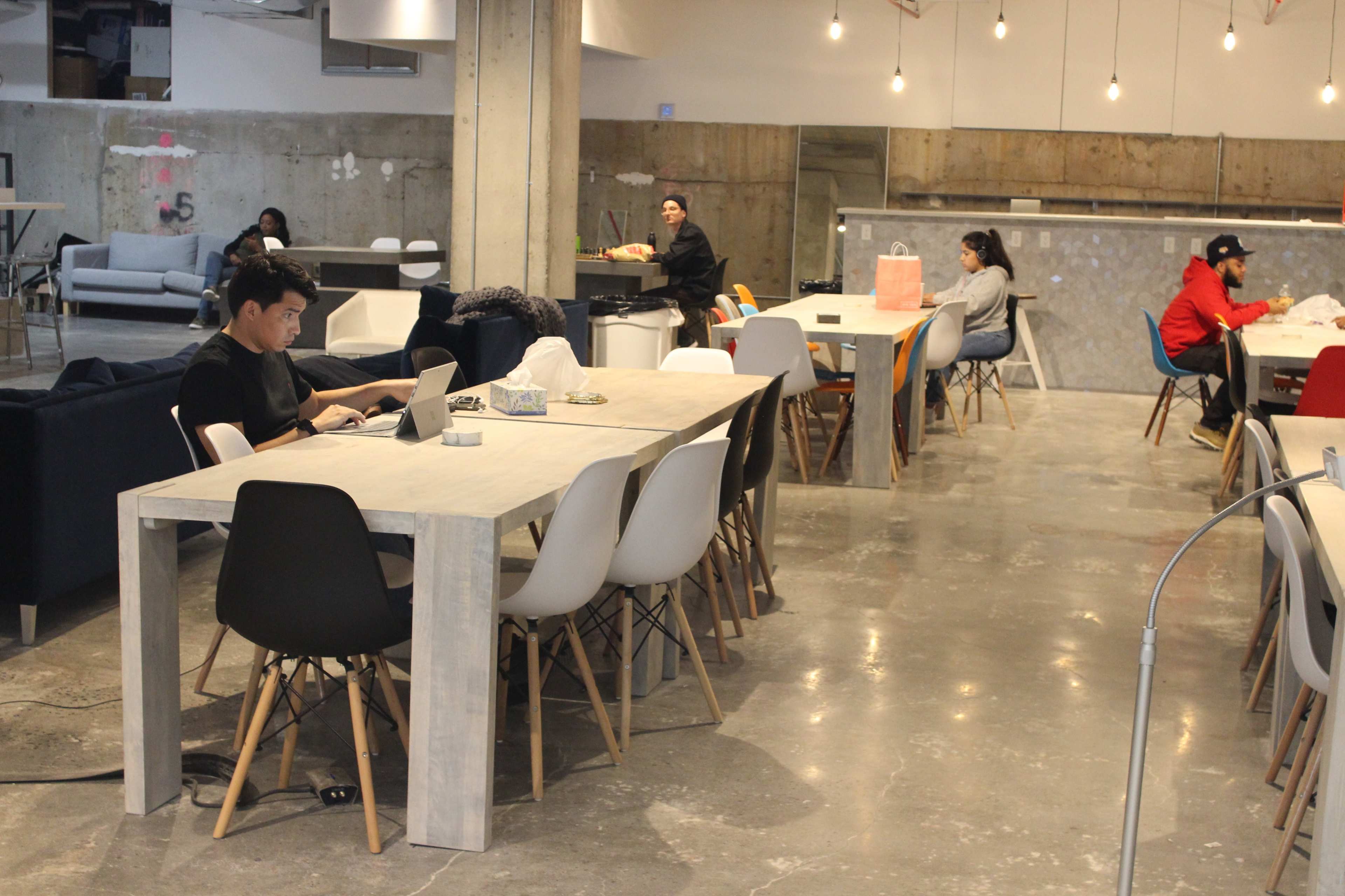 A spacious open area with several tables and chairs, where individuals are working or studying at different locations.
